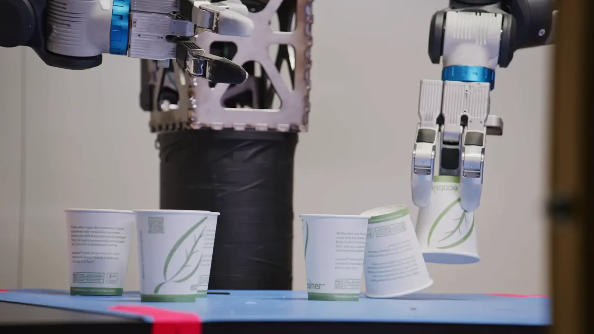 The Atlas robot's three-fingered hand gently grips a stack of white paper cups, showcasing its ability to handle delicate objects.