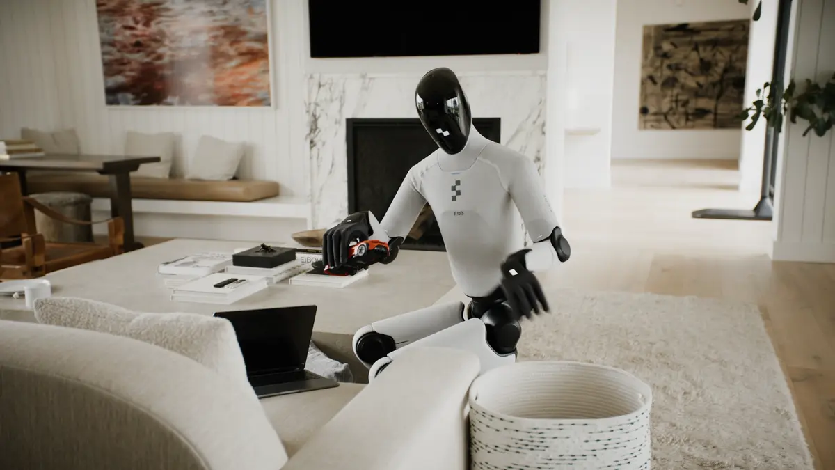A Figure 03 humanoid robot kneels on the floor in a modern living room, picking up children's toys from a coffee table and placing them in a basket.