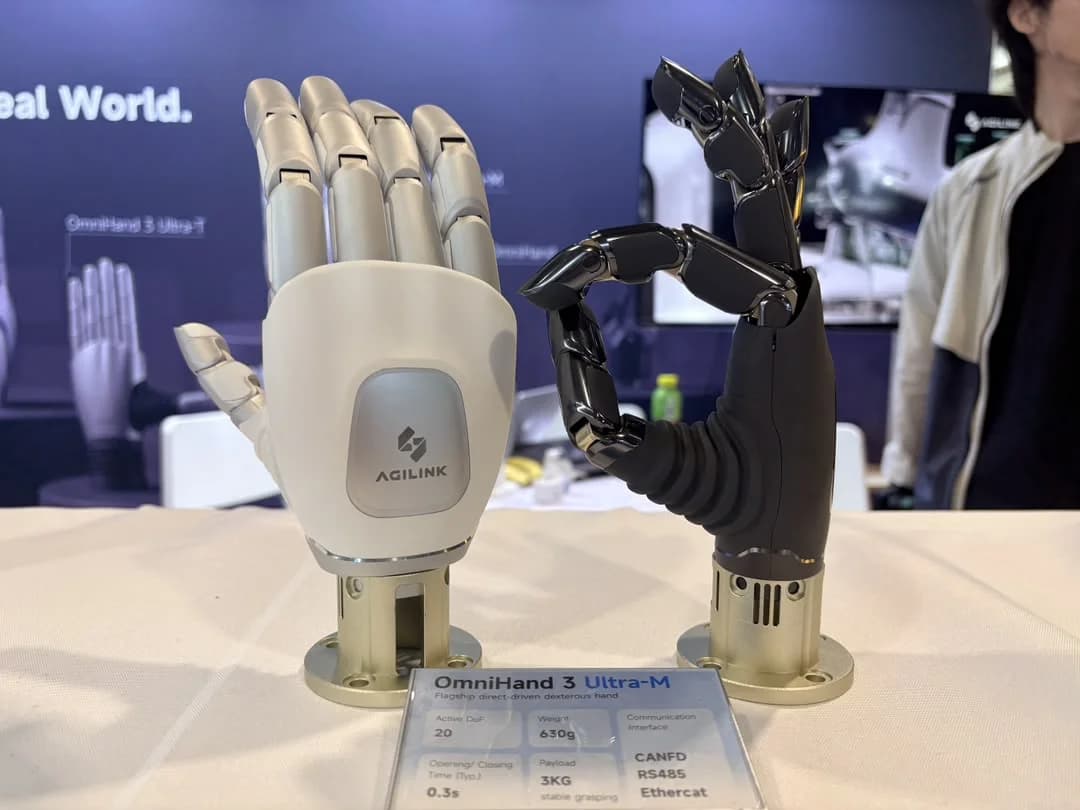 Two OmniHand 3 Ultra-M robotic hands displayed on table stands. The left hand is matte white with an open palm facing forward, while the right hand is matte black, forming an OK gesture with its fingers.