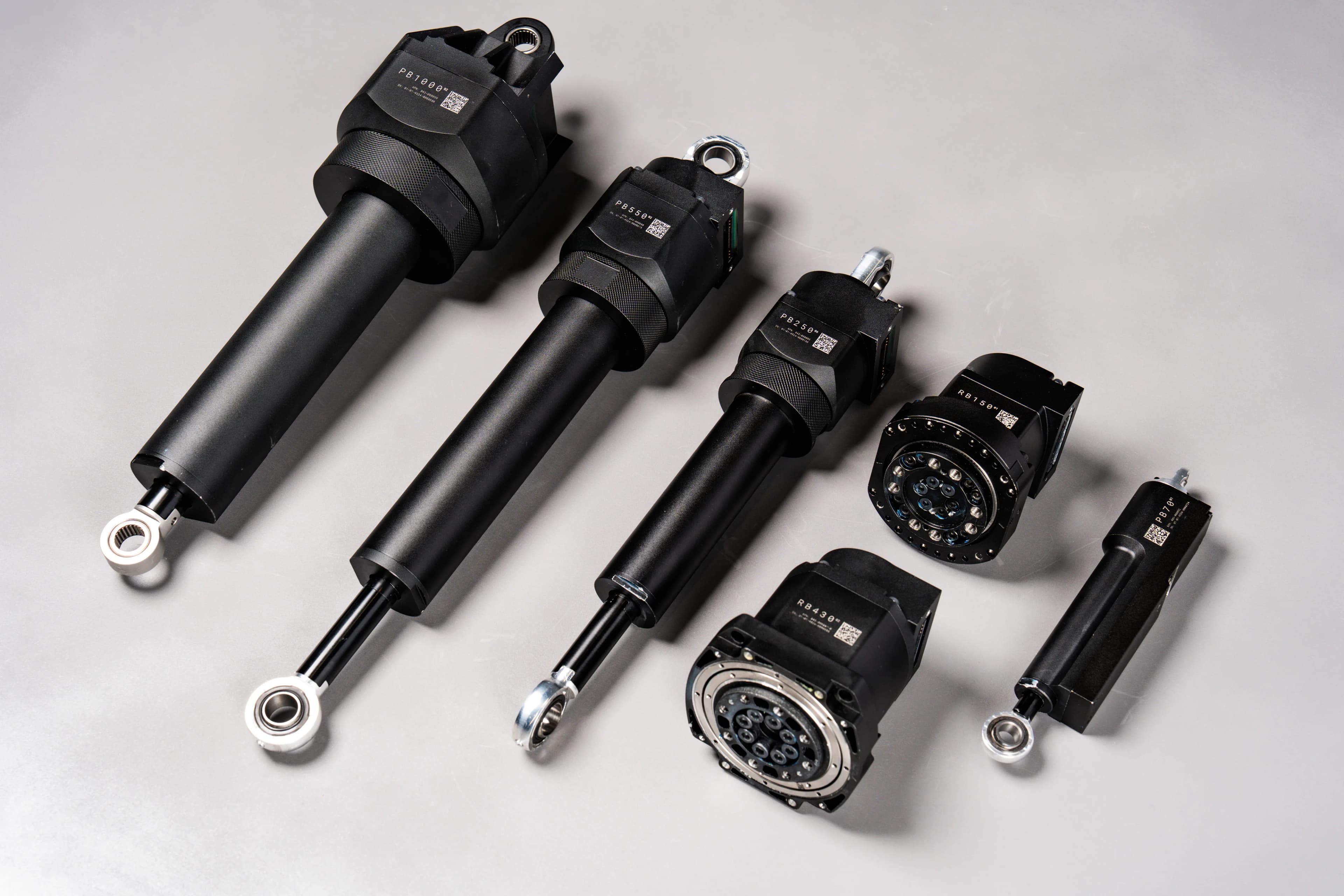 Six variations of Apptronik's patented black linear and rotary robotic actuators arranged neatly in a diagonal row on a smooth grey background.