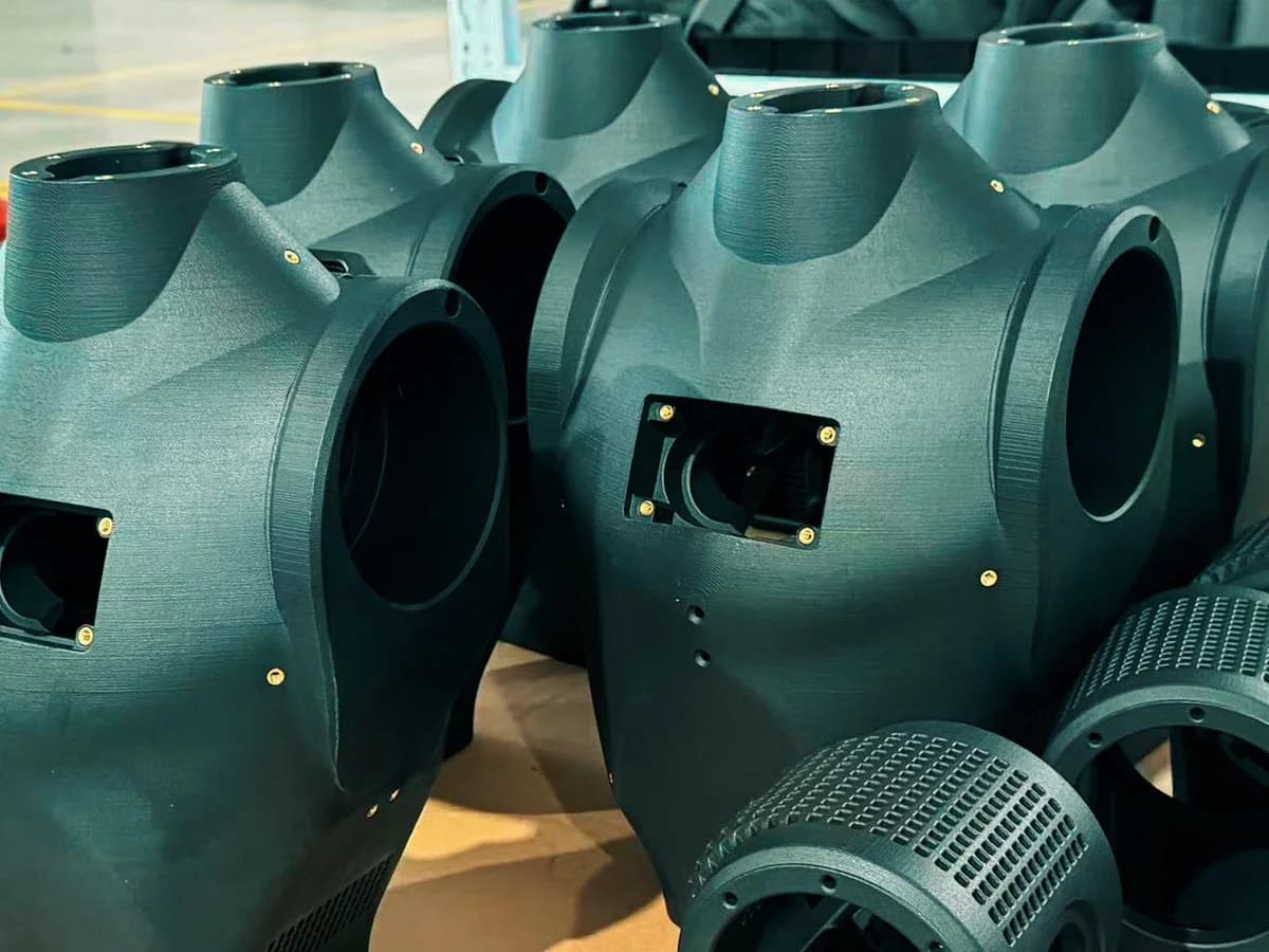 Multiple matte black 3D-printed Asimov 1 humanoid torso and housing shells lined up in a workshop, showing brass threaded inserts and cutouts for sensors and actuators.