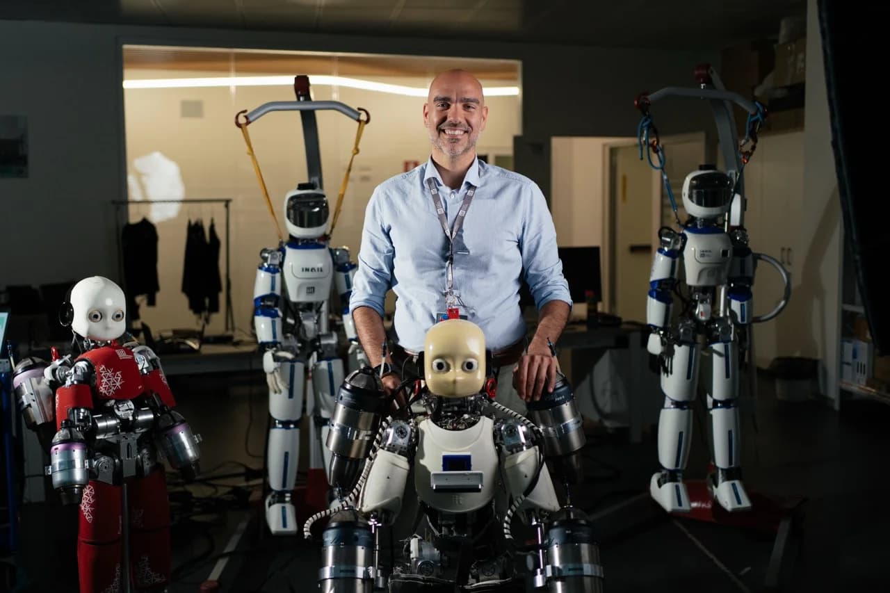 CEO Daniele Pucci smiling in a lab, standing behind a robot with jet engines attached to its arms, flanked by two other white and blue humanoid robots.