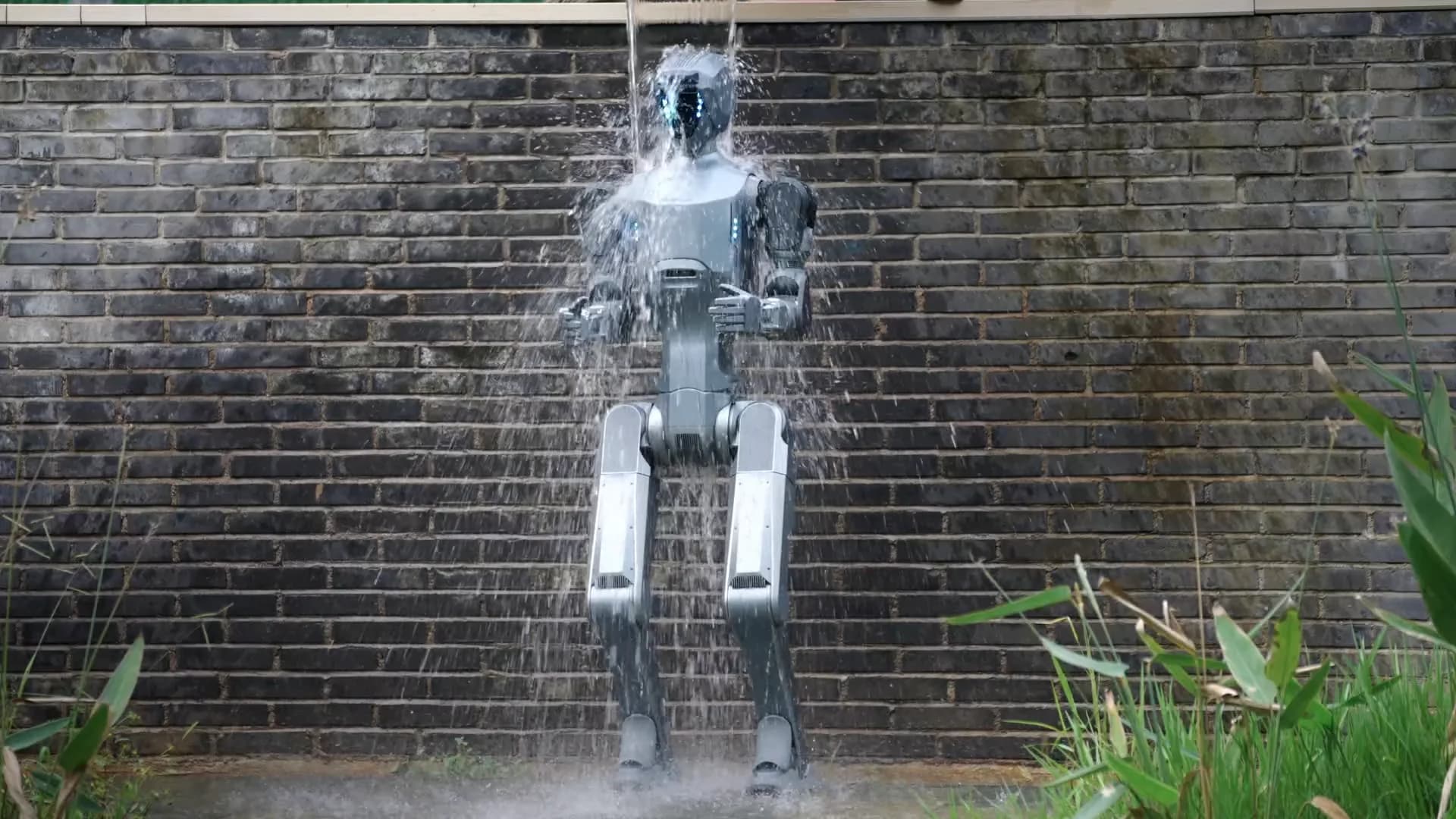 The Deep Robotics DR02 humanoid robot standing under a heavy stream of water in front of a brick wall, demonstrating its all-weather durability.