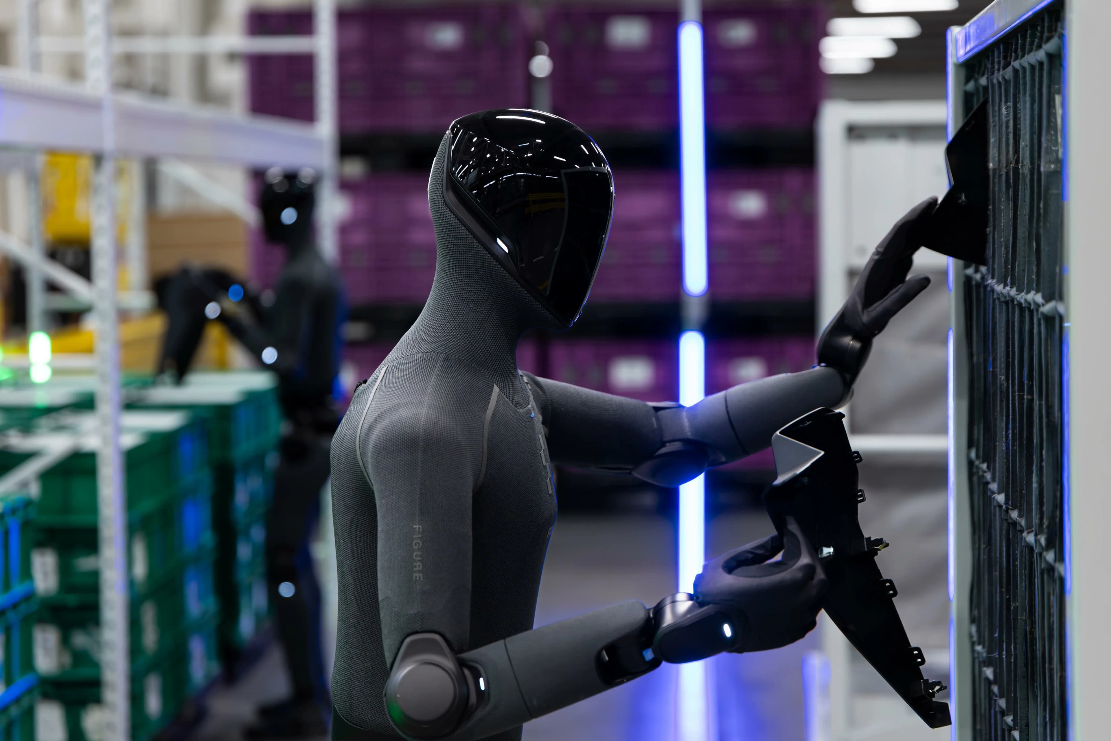 A close-up profile shot of a Figure 03 humanoid robot using both of its hands to insert a complex black plastic automotive piece into a shelving unit, with a second blurry robot visible in the background.