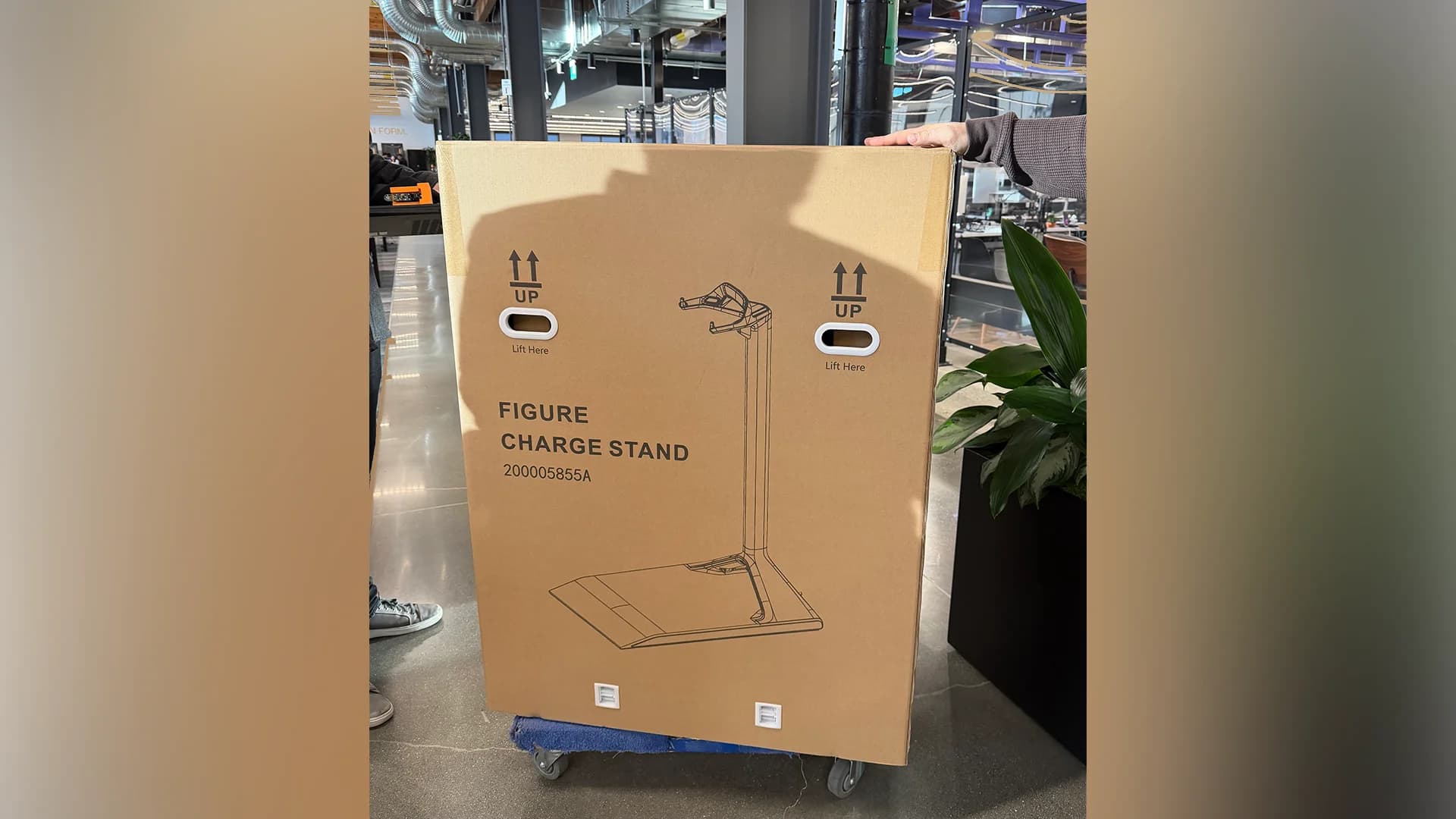 A large cardboard shipping box labeled "FIGURE CHARGE STAND" with a line drawing of the hardware.