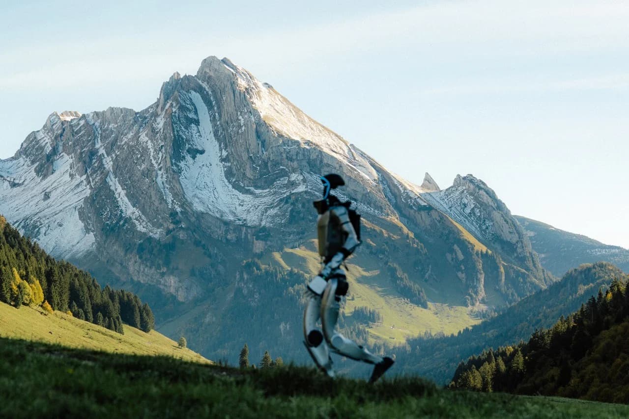 A Unitree G1 humanoid robot walking in the foreground with a towering Swiss Alp mountain peak rising in the background.