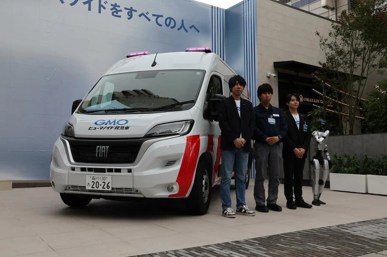 GMO AI and Robotics team standing beside the front of the Fiat Humanoid Ambulance with pink emergency lights and a bipedal robot