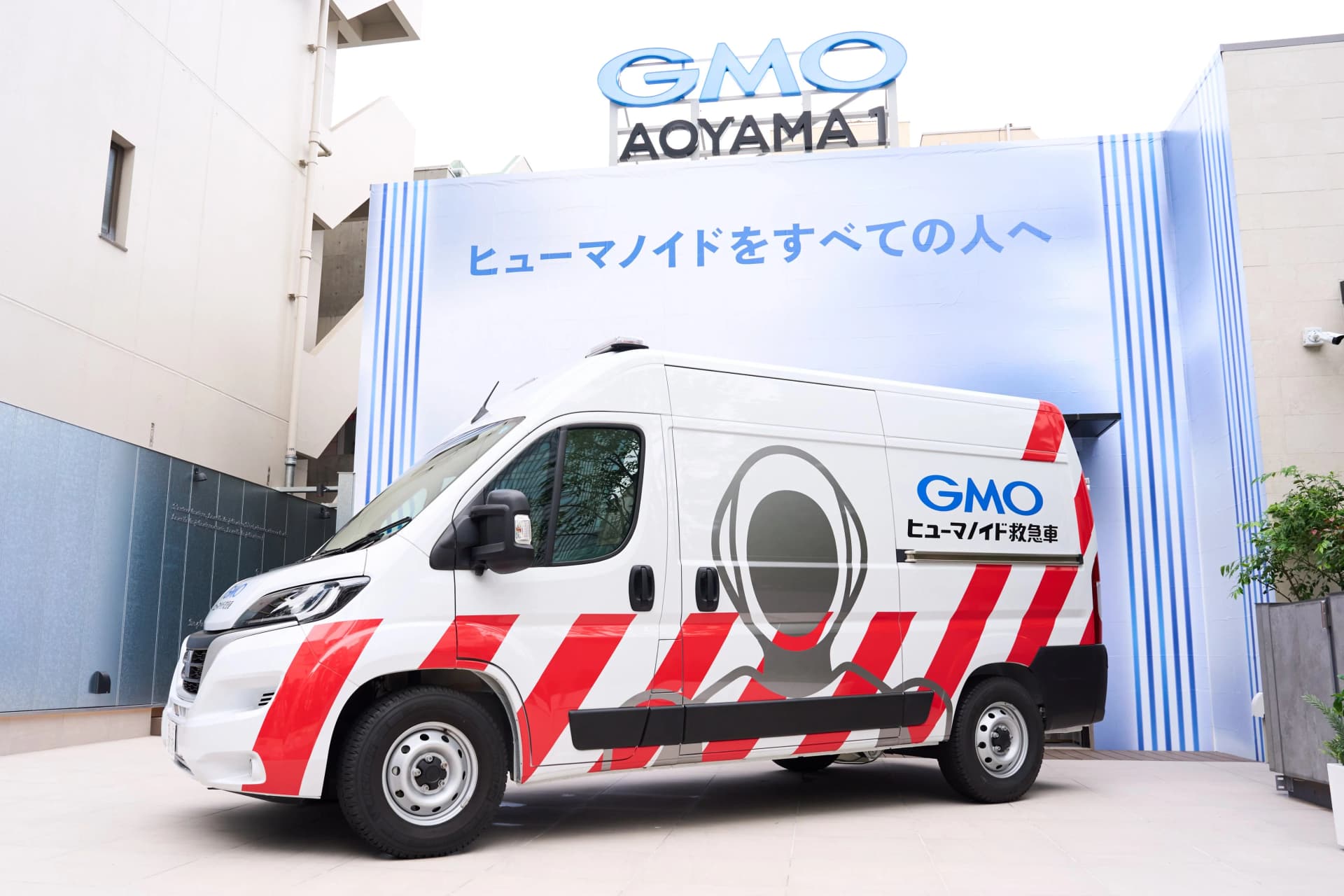Side view of the white GMO Humanoid Ambulance van featuring red diagonal emergency stripes and humanoid robot branding