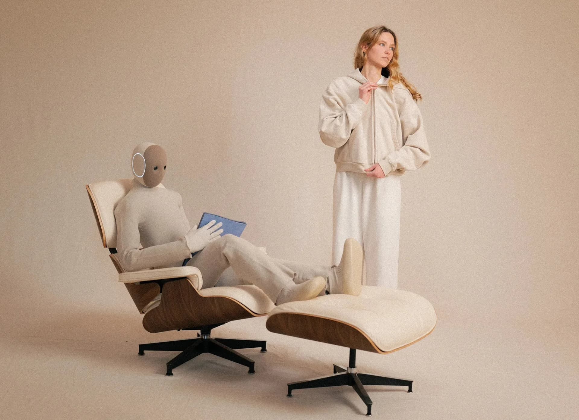 A NEO robot lounging in a classic Eames-style lounge chair with its feet up on an ottoman, holding a blue book.