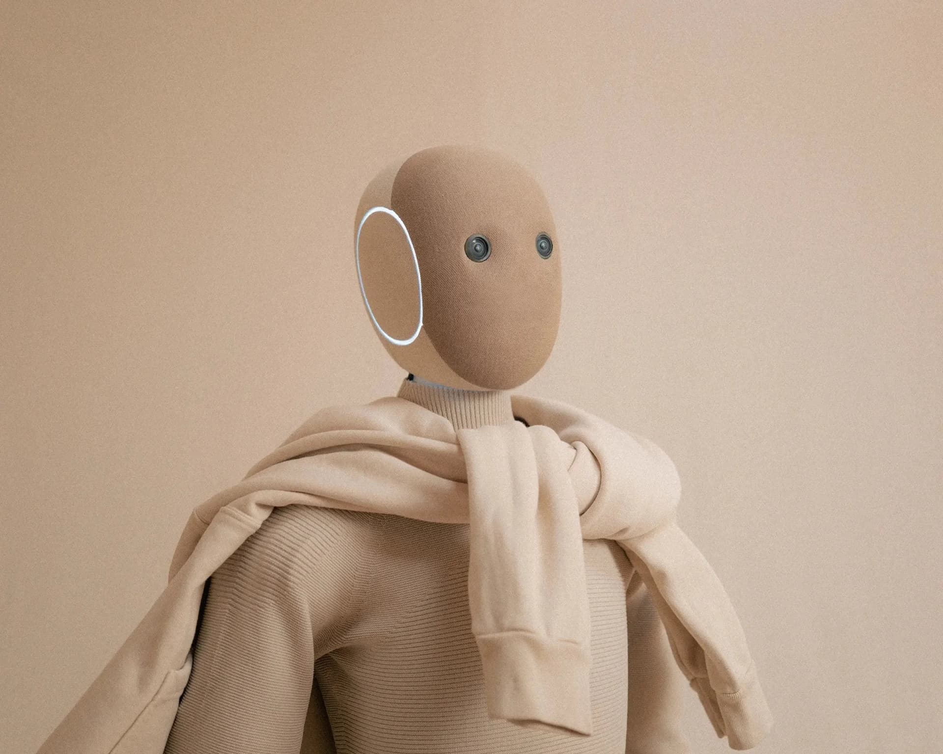 The NEO humanoid robot wearing a beige zip-up hoodie, showing the fabric's soft texture and the robot's camera eyes.