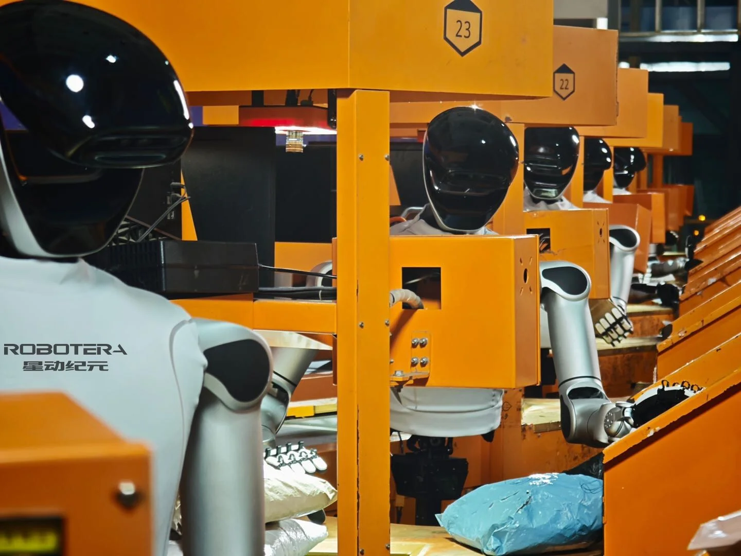 A fleet of Robotera L7 humanoid robots with black visor heads and silver bodies working at orange industrial conveyor workstations in a logistics warehouse.