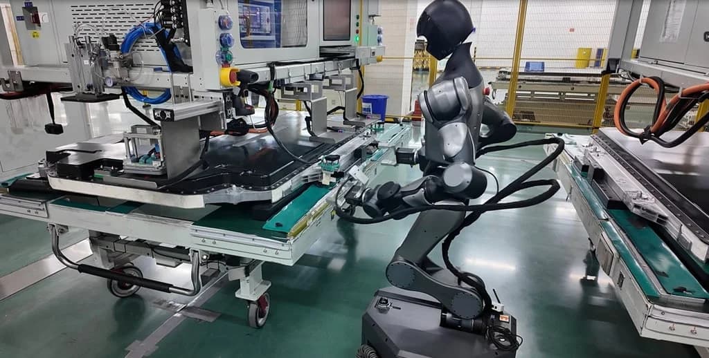 A Spirit AI robot operating on a factory production line. The robot has a humanoid upper body but is mounted on a wheeled mobile base for stability. It is shown reaching into a large black EV battery pack to perform a connector insertion task.