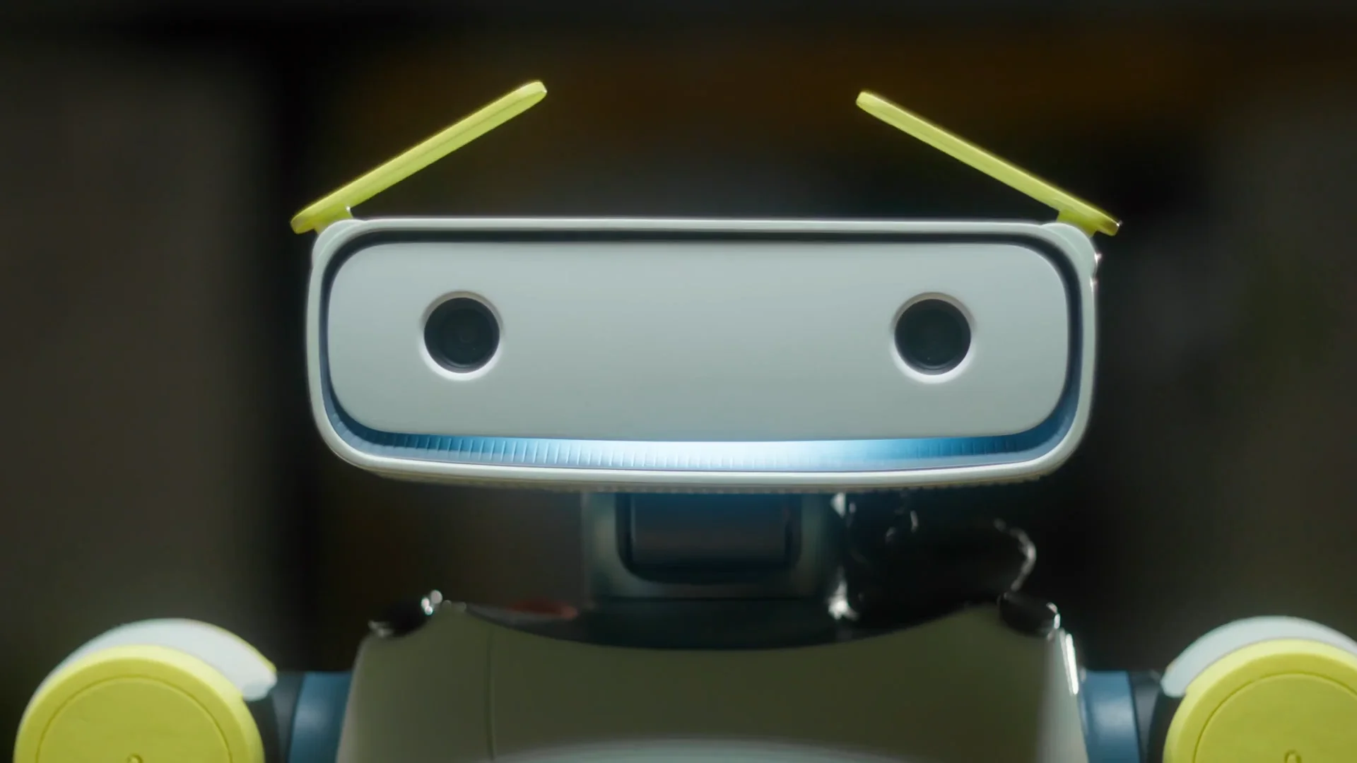 A close-up of the Sprout robot's head, featuring a white rectangular face with two black camera lenses, a blue glowing light strip at the bottom, and two yellow, angled eyebrows on top.