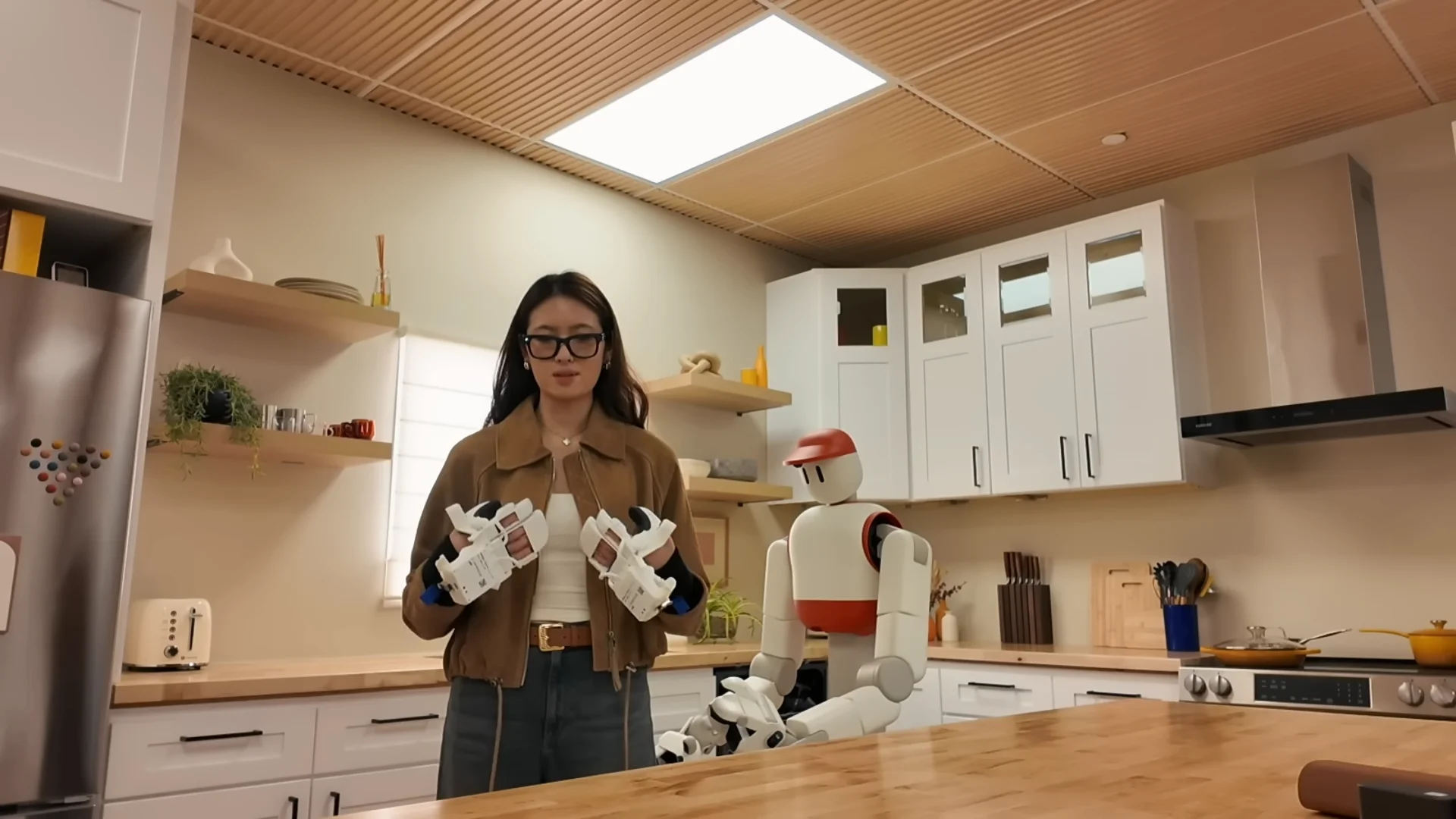 Claire Zau wearing a pair of white and black Skill Capture Gloves while standing in a kitchen setting next to a Memo robot.