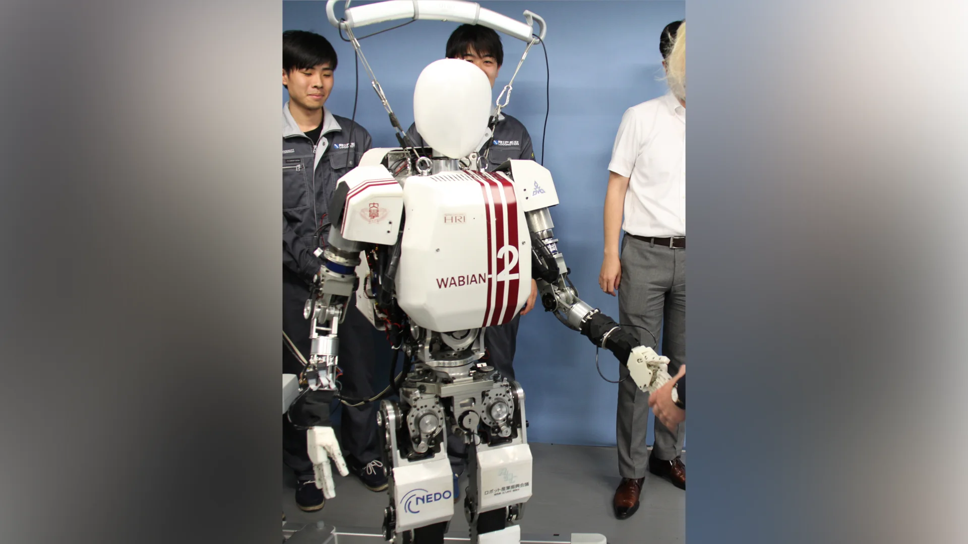 A white humanoid robot with red stripes, labeled WABIAN-2, standing in a lab with Japanese researchers in the background.