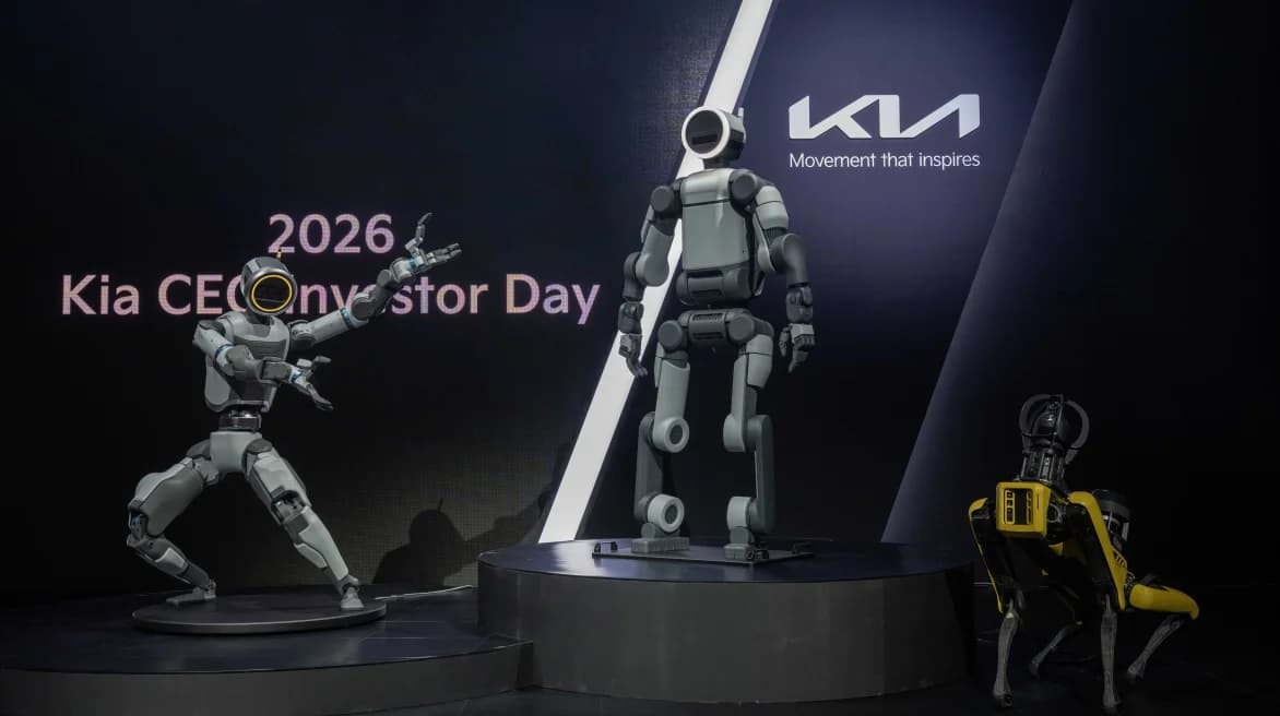 Three Boston Dynamics robots—a prototype Atlas in a dynamic pose, a production-ready Atlas, and a yellow Spot quadruped—standing on a stage at the 2026 Kia CEO Investor Day.