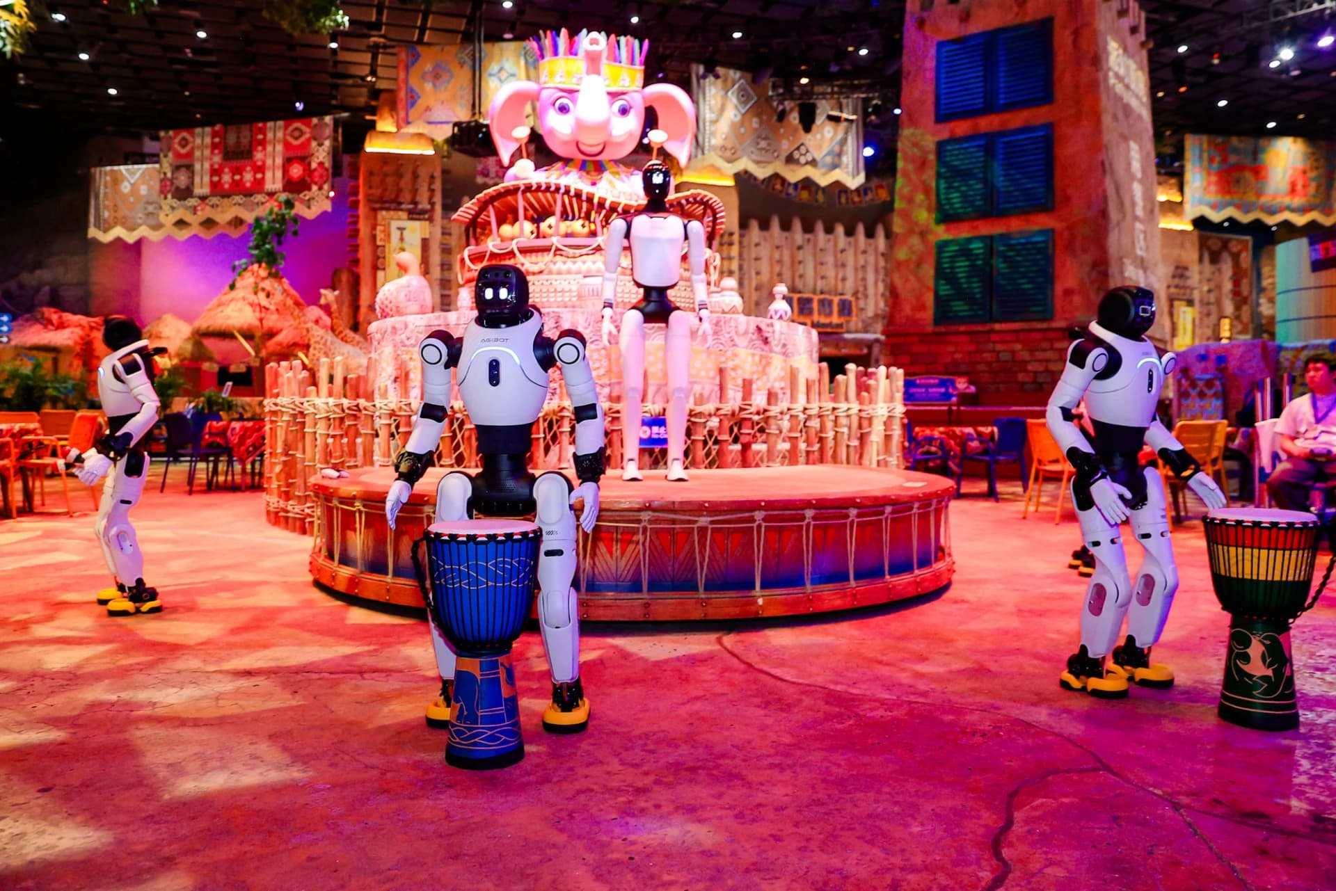 AGIBOT humanoids arranged around drums in a colorful themed performance area at Chimelong.