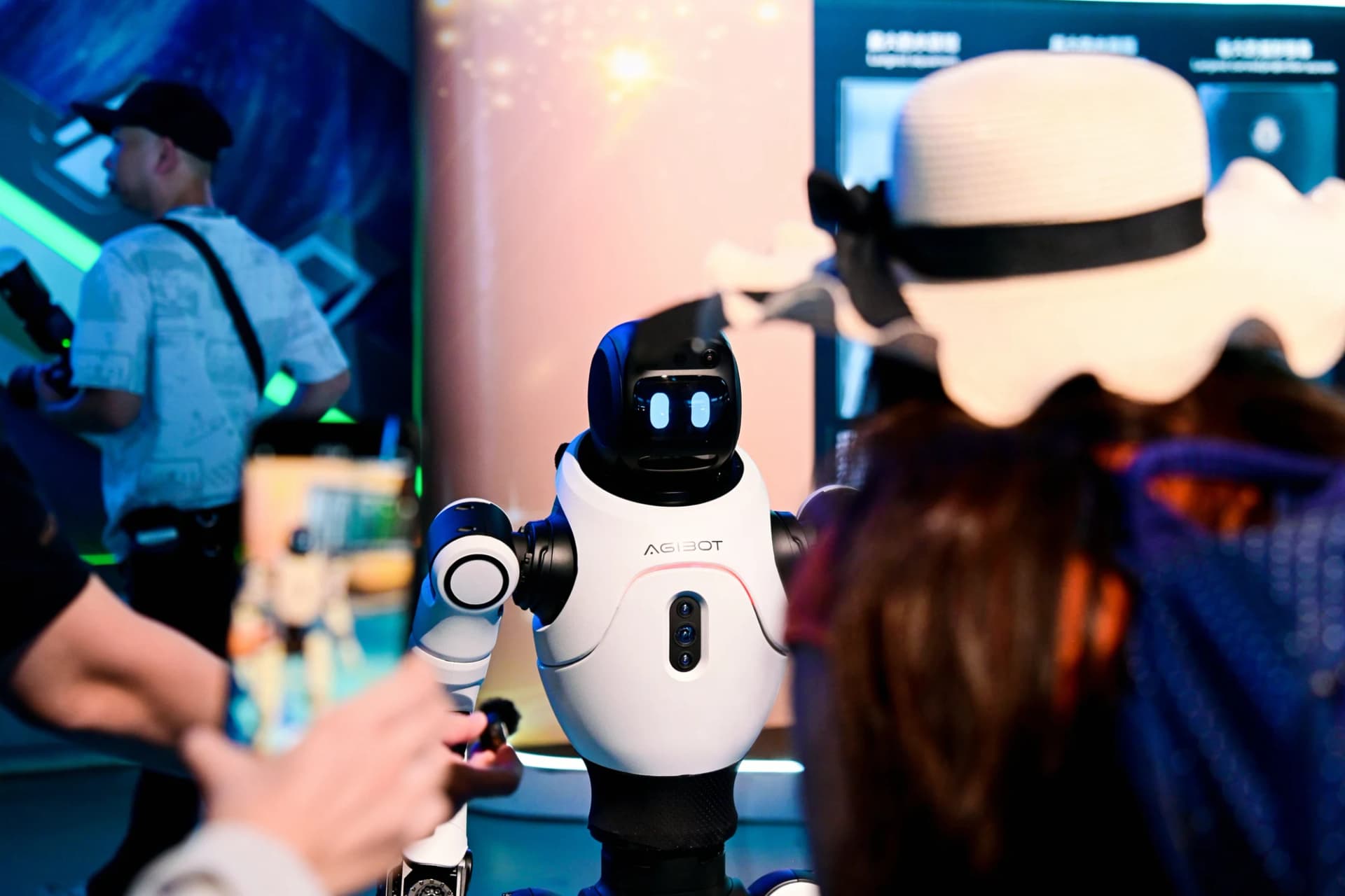 An AGIBOT X2 robot faces visitors, with one person holding up a phone to photograph it.