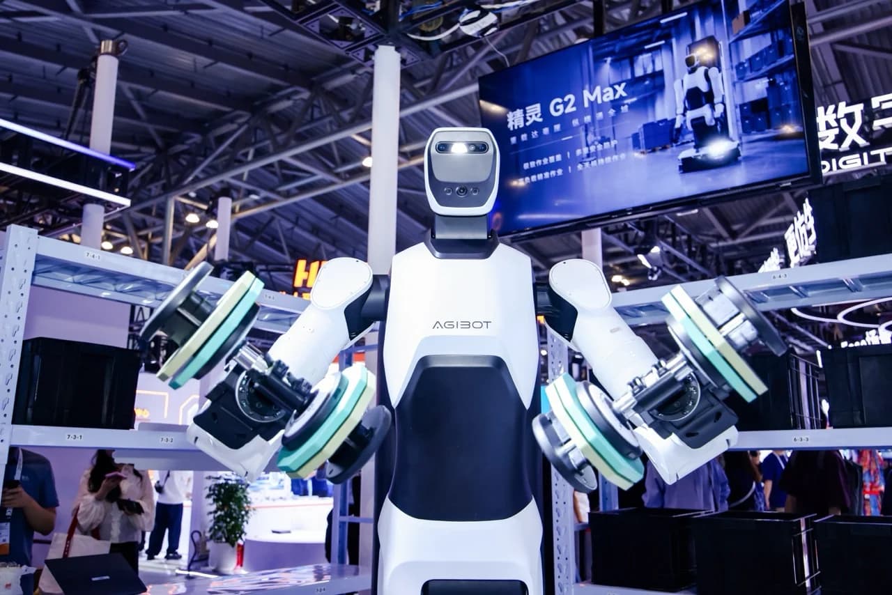 An AGIBOT G2 Max heavy-payload industrial robot holding heavy industrial components with both dual-arm effectors in front of warehouse shelving.