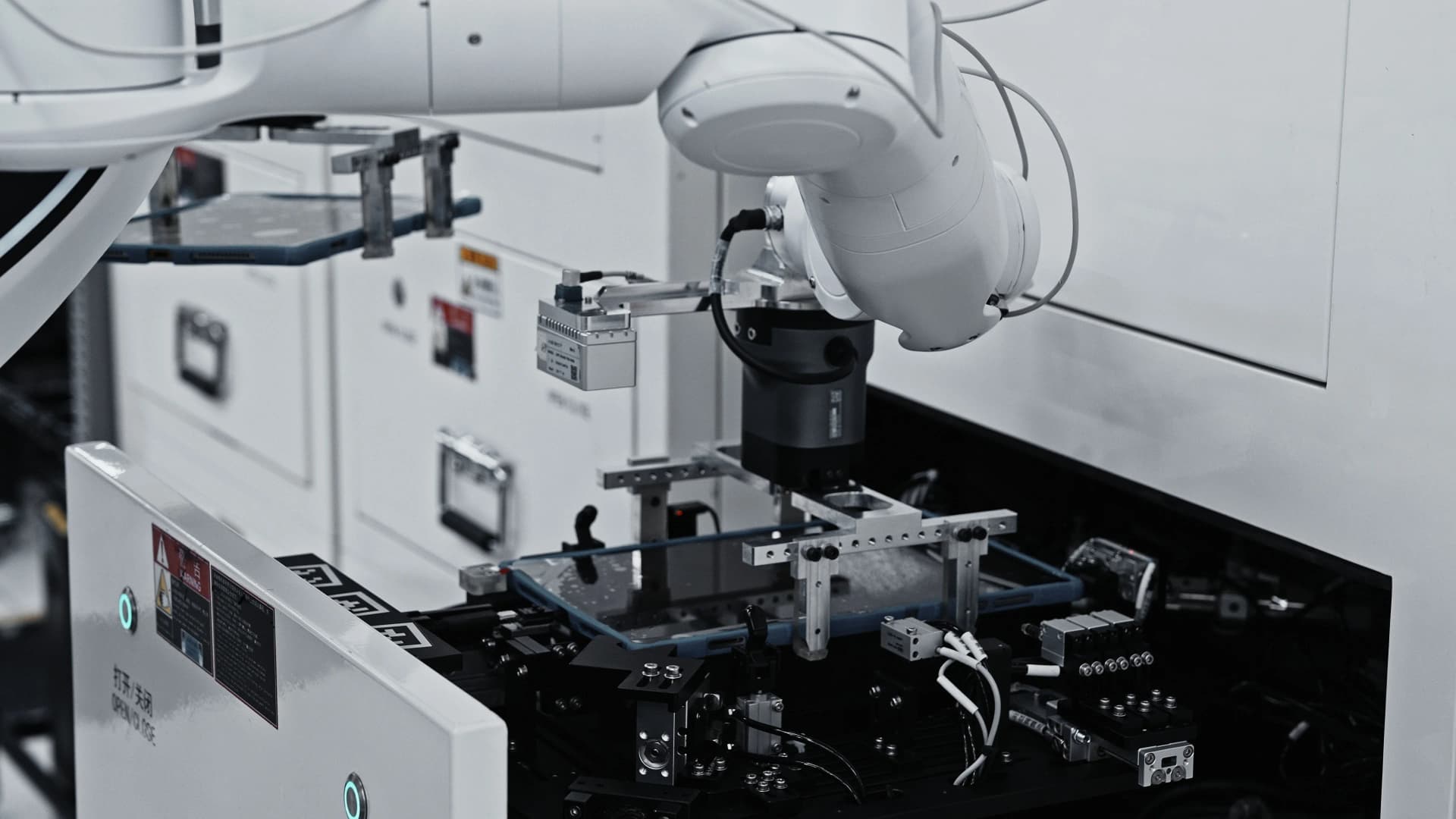 Close-up of an AGIBOT G2 robotic arm using a precision vacuum gripper to place a tablet into a testing fixture.