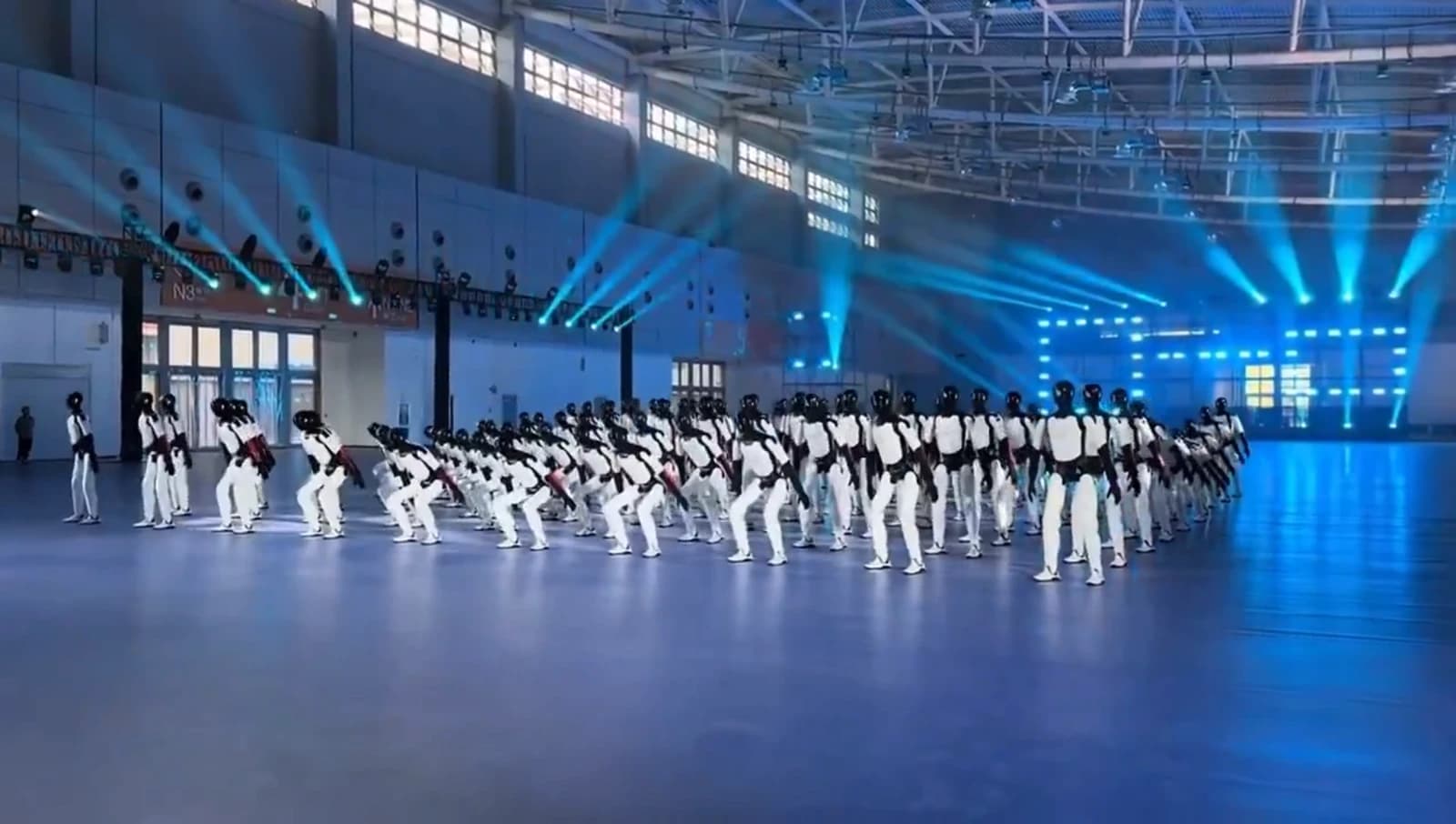 Rows of AGIBOT humanoid robots performing a synchronized routine under blue lights in an exhibition hall.