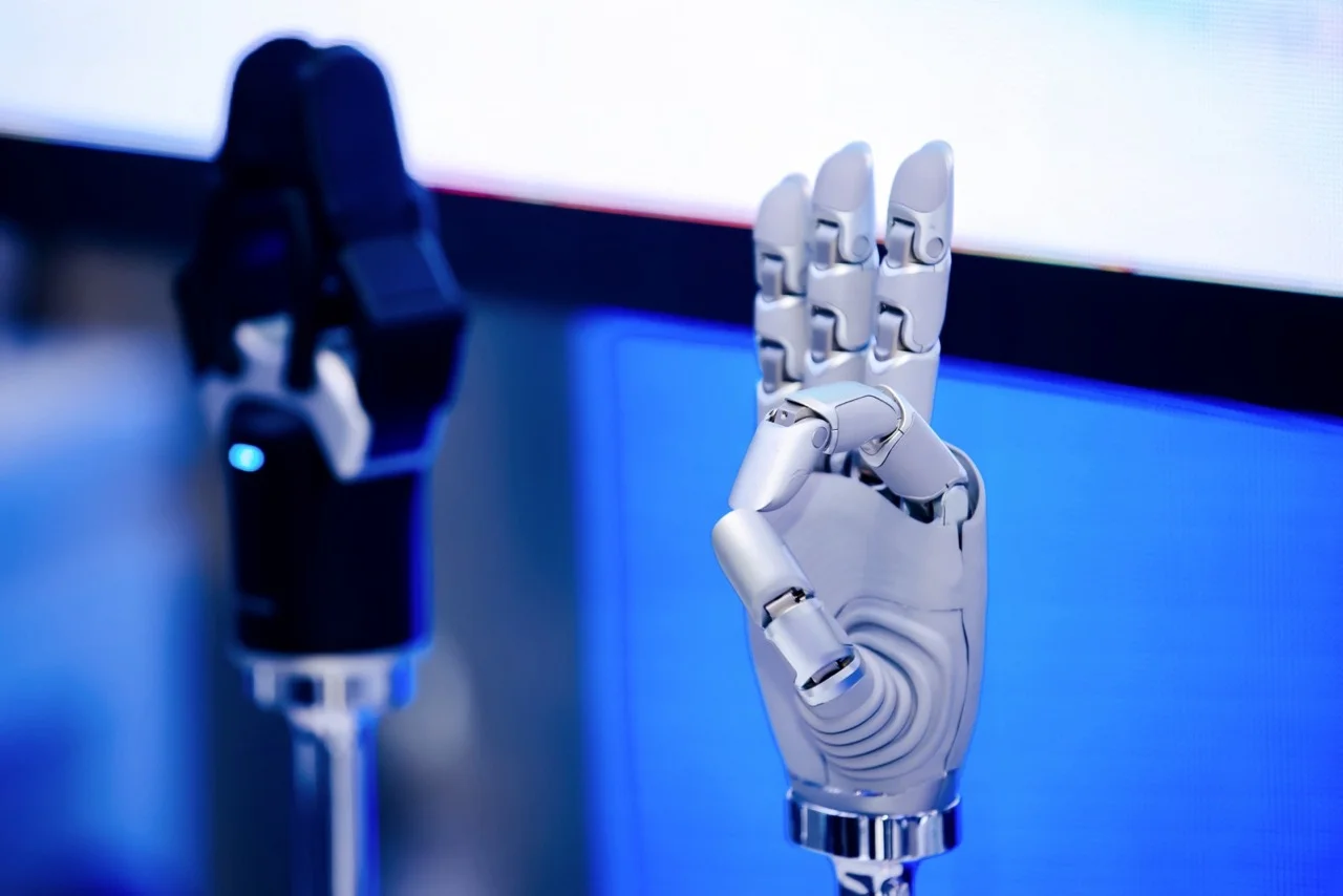 A silver metallic AGIBOT OmniHand 3 Ultra-M dexterous robotic hand mounted on a stand, forming an OK gesture with its index finger and thumb touching.