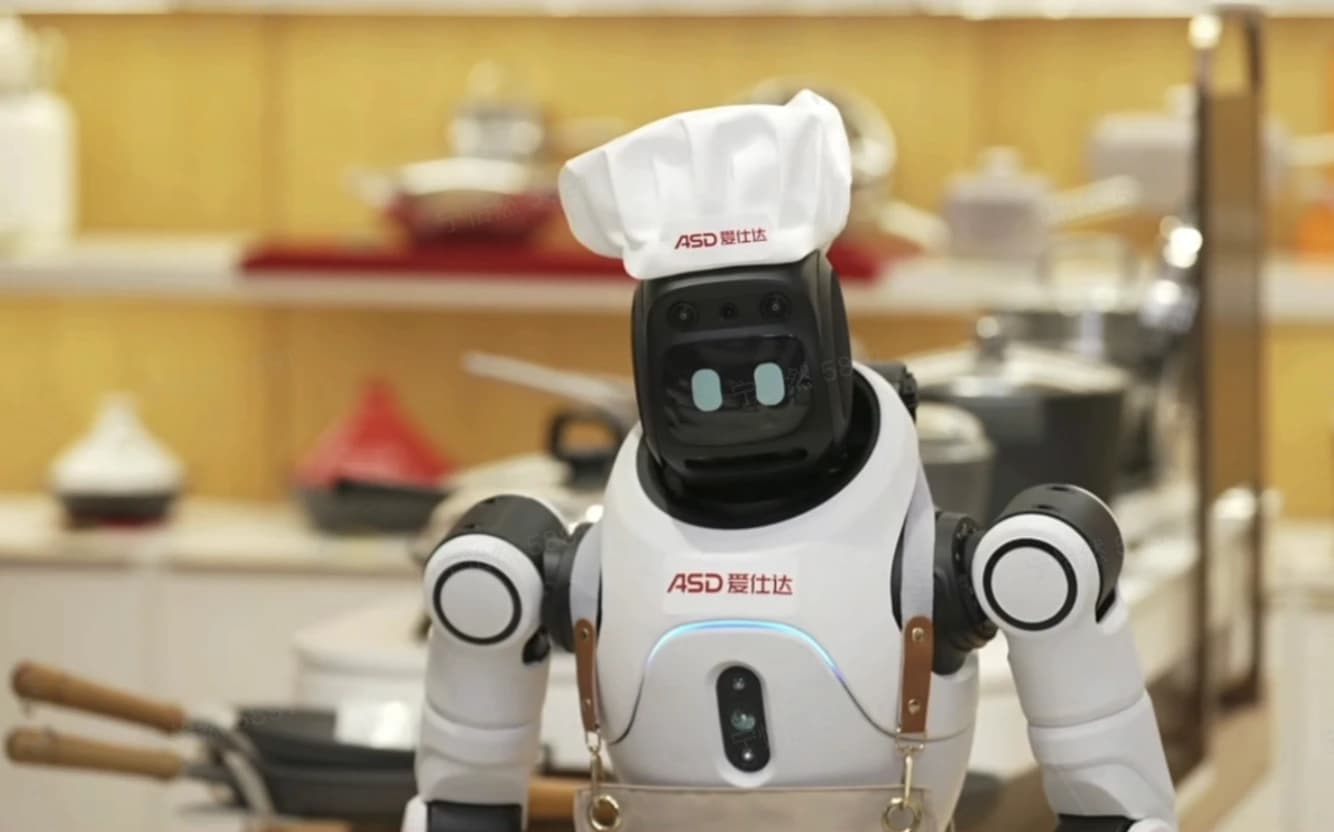 AGIBOT X2 humanoid wearing an ASD-branded chef’s hat and apron in front of cookware displays.