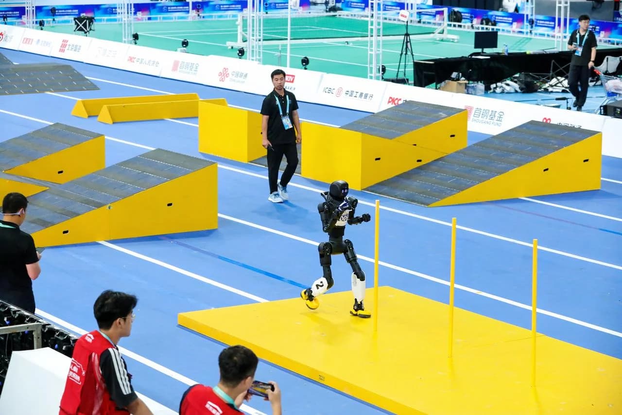 A black and white bipedal AGIBOT X2 humanoid robot with yellow feet navigating an obstacle course featuring yellow ramps and vertical slalom poles on a blue indoor track, watched closely by event staff.