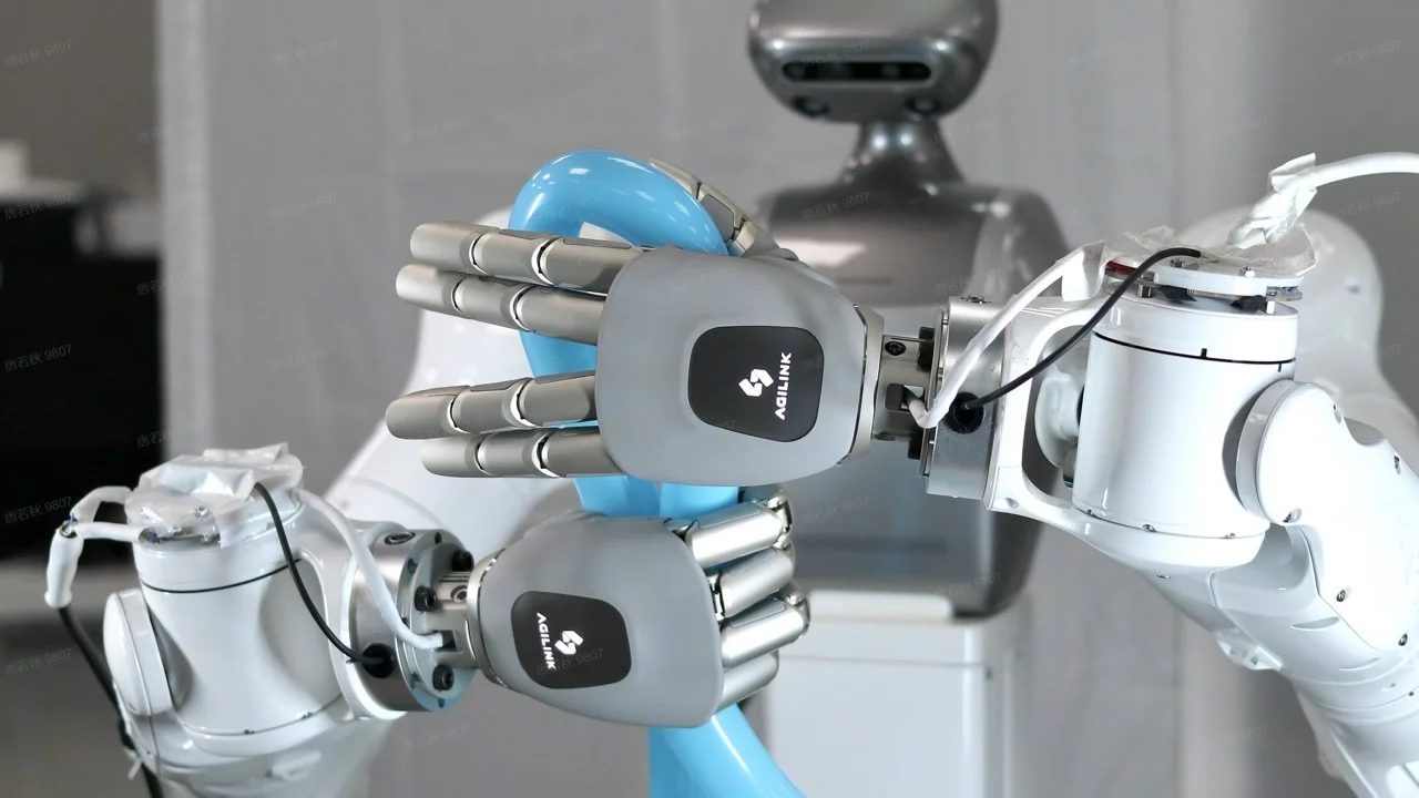 A pair of robotic hands carefully manipulating a blue balloon, with the blurred silver torso and head of a humanoid robot visible in the background.