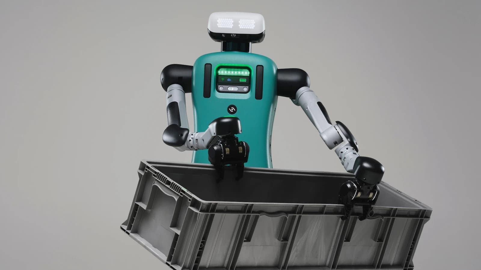 Agility Robotics Digit humanoid holding a gray tote against a neutral background.
