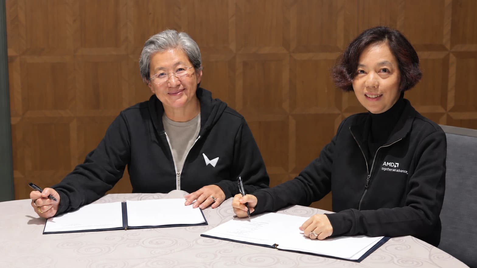 Two executives seated at a table with pens and open document folders at the AMD–World Labs signing.