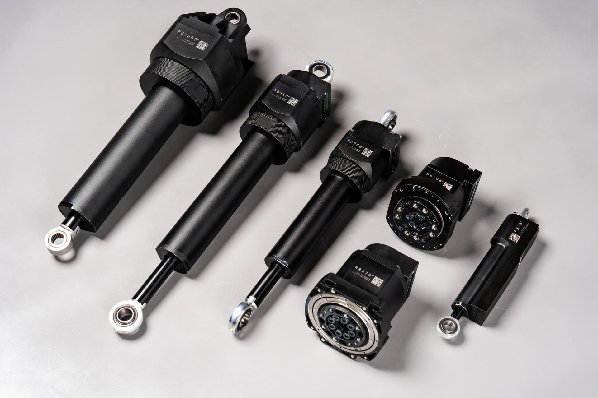 Six variations of Apptronik's patented black linear and rotary robotic actuators arranged neatly in a diagonal row on a smooth grey background.