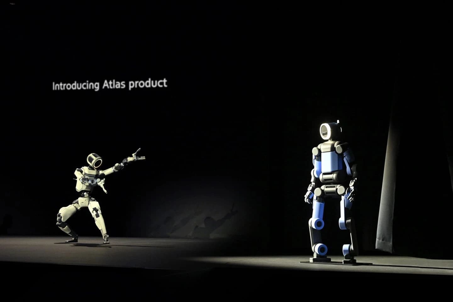 The blue production Atlas stands on the right of a CES 2026 stage while the research Atlas poses on the left beneath the words Introducing Atlas product.