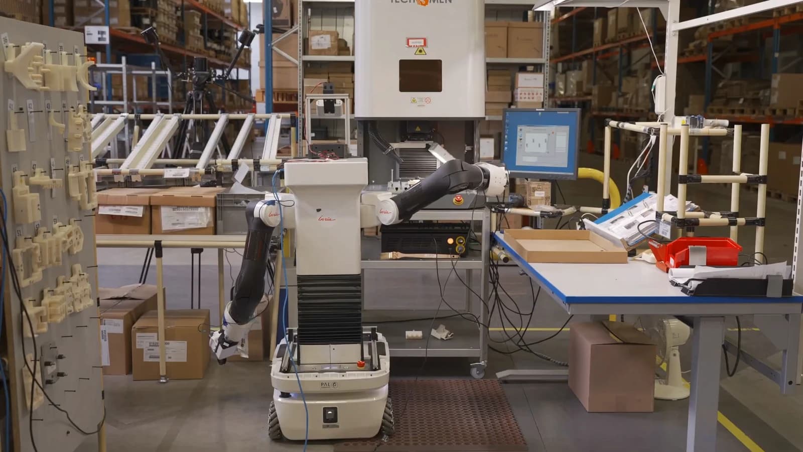 Dual-arm mobile robot reaching toward an engraving machine in an industrial workstation.