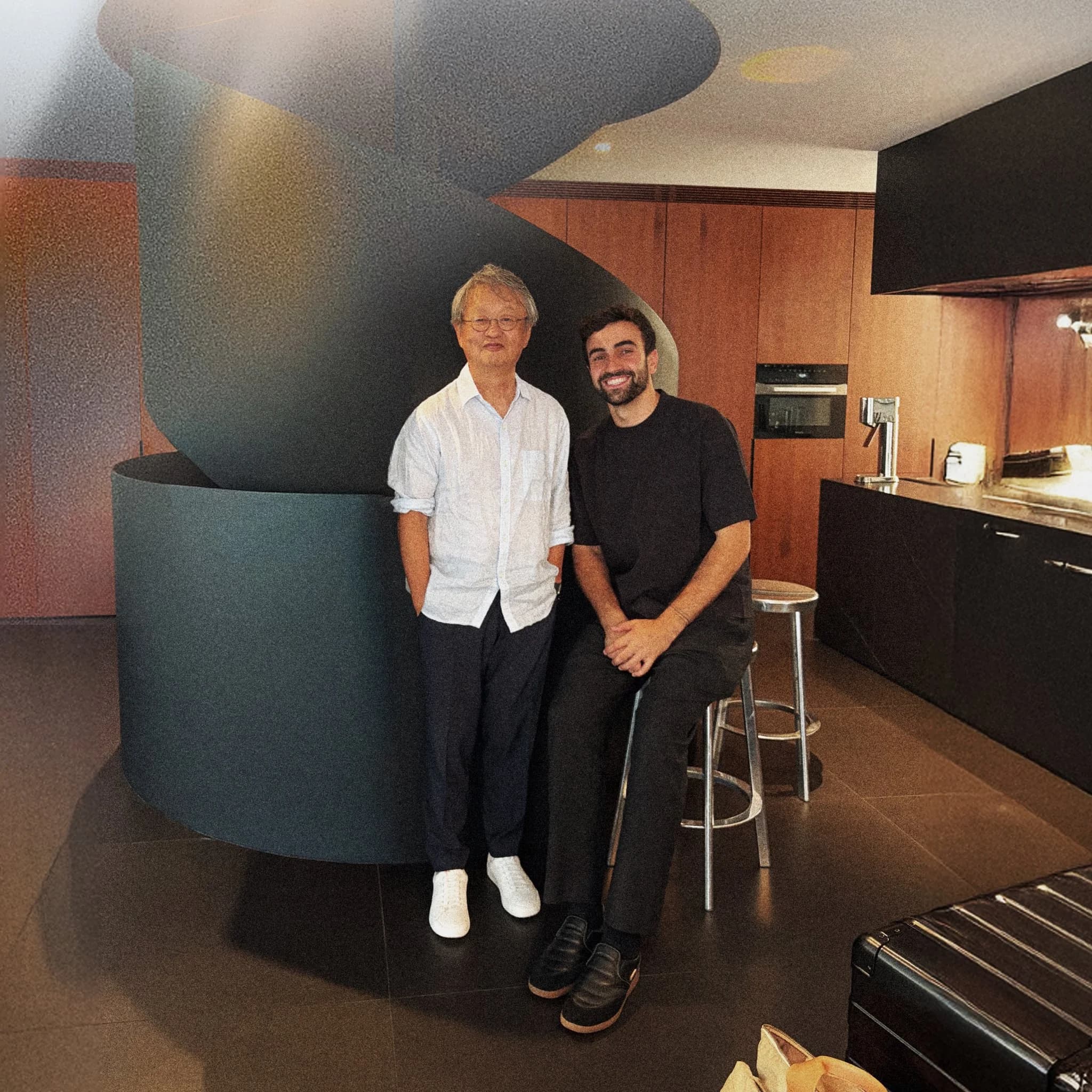 1X Chief Designer Dar Sleeper sitting beside Japanese industrial designer Naoto Fukasawa inside a minimalist modern design studio.