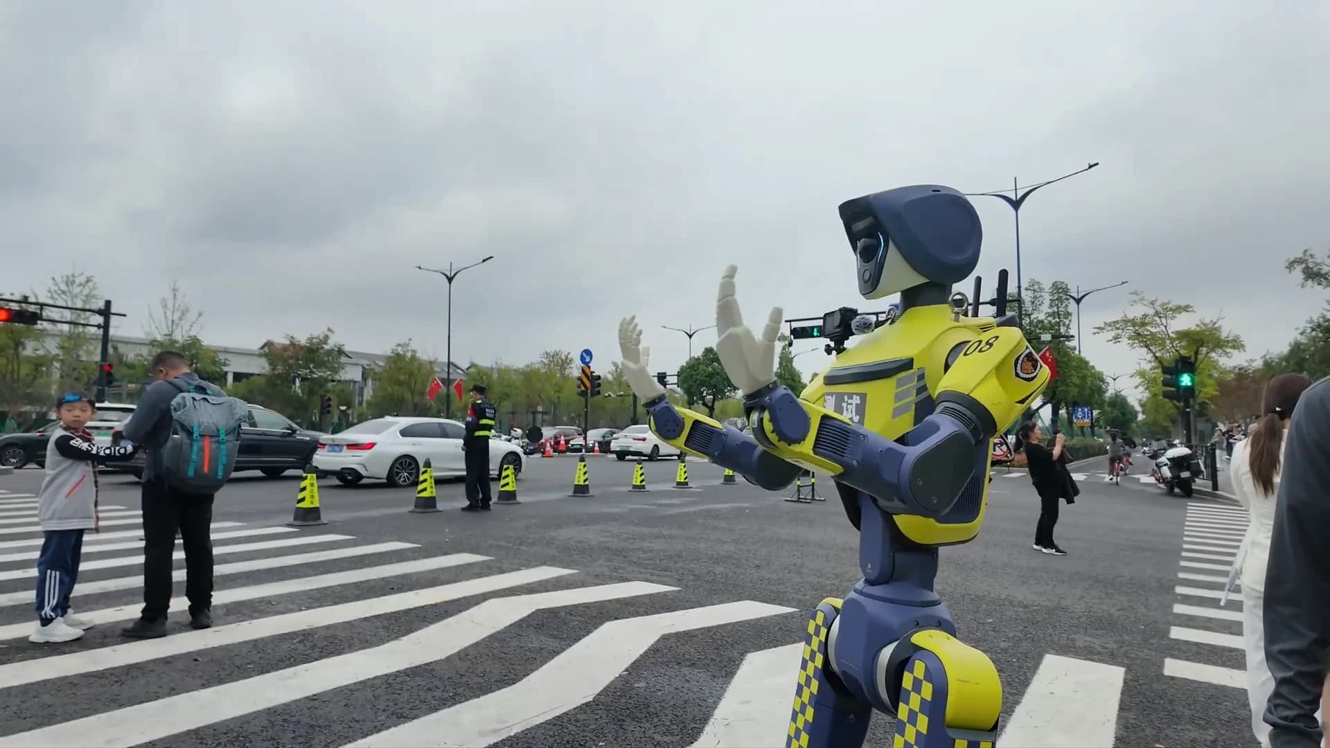 A yellow-and-blue DR02 humanoid making traffic gestures at a street crossing.