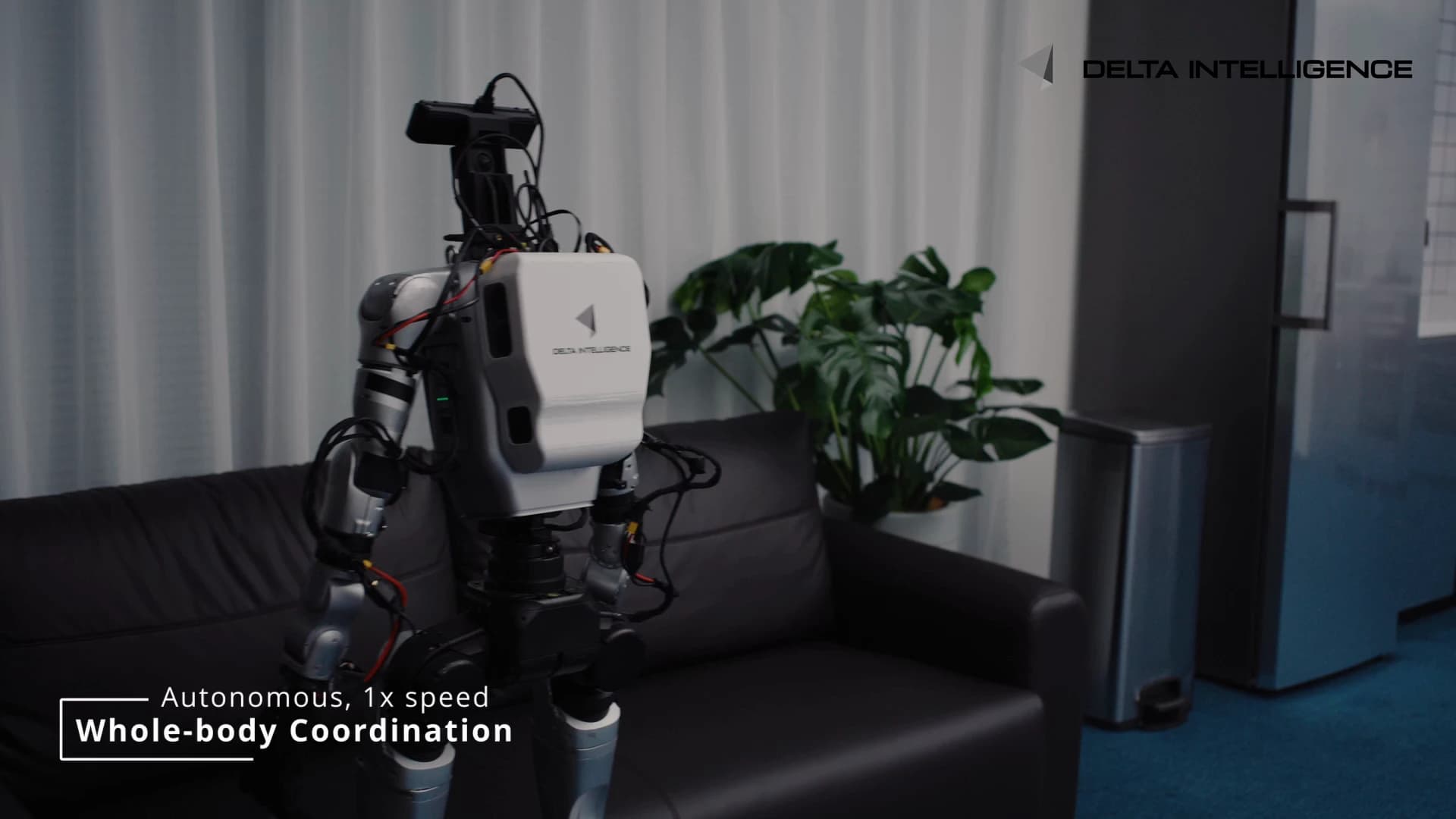 Rear view of a humanoid robot with a white Delta Intelligence backpack and a camera-equipped head beside a sofa.