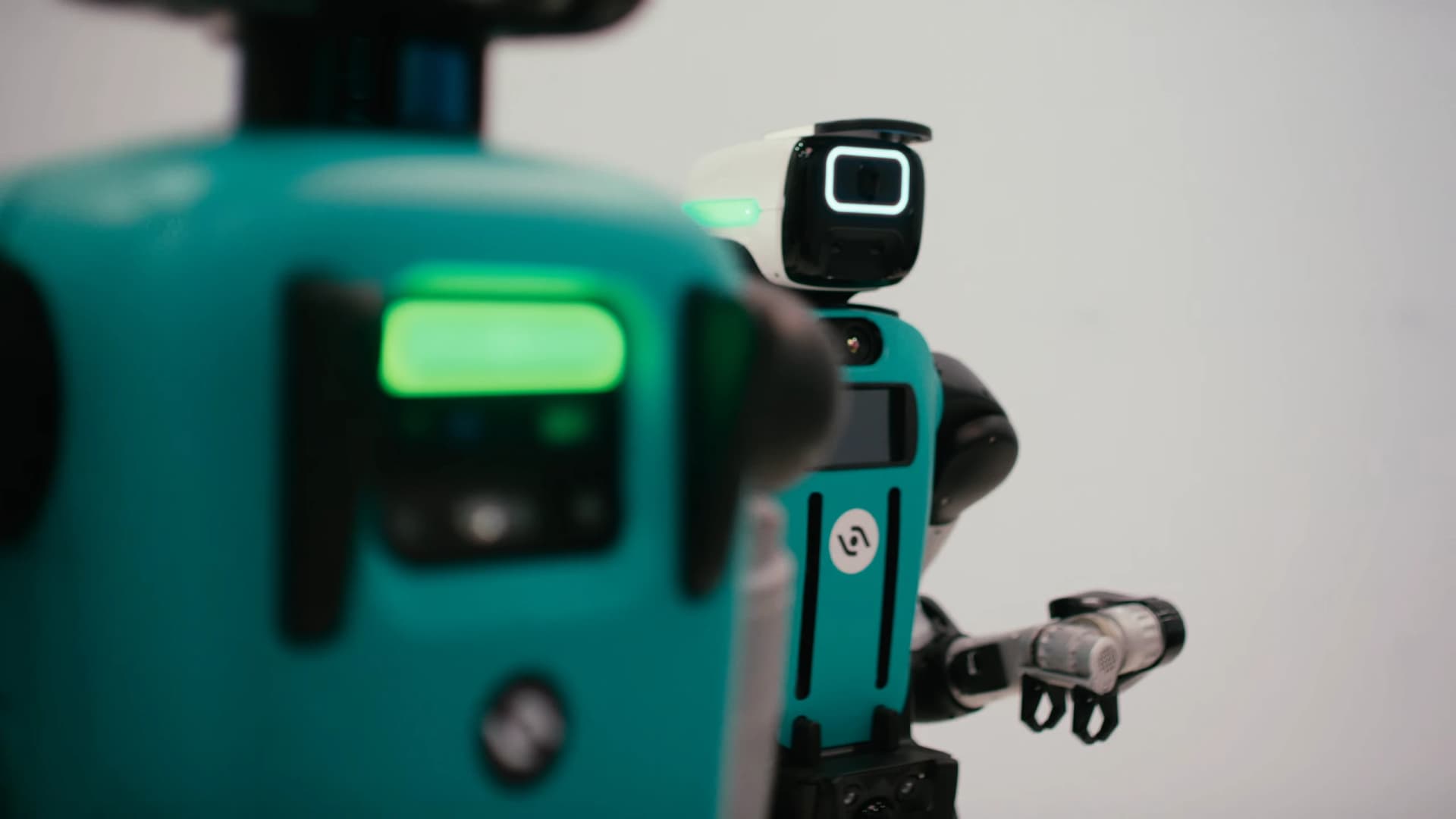 Two teal Digit 5 humanoid robots, with one in focus and the other blurred in the foreground.