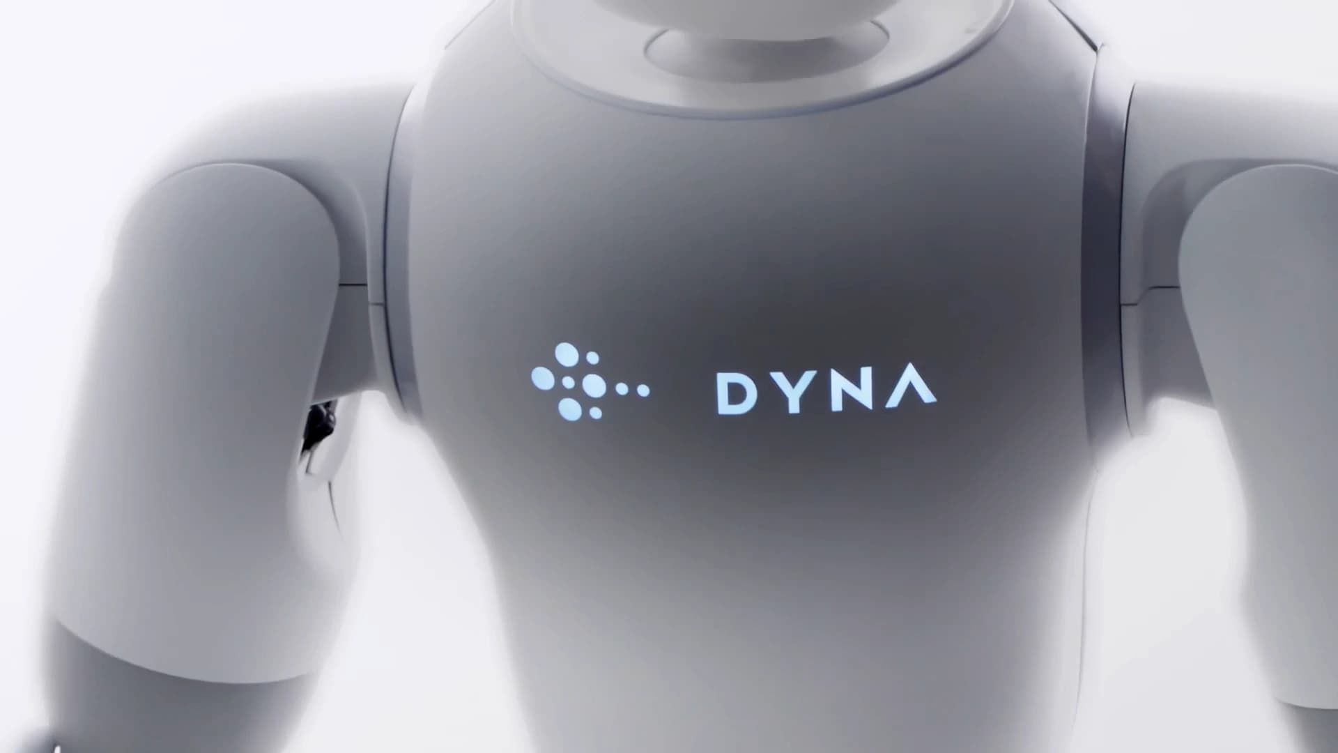 Close-up of a gray robot’s torso and shoulders, with an illuminated Dyna logo on its chest.