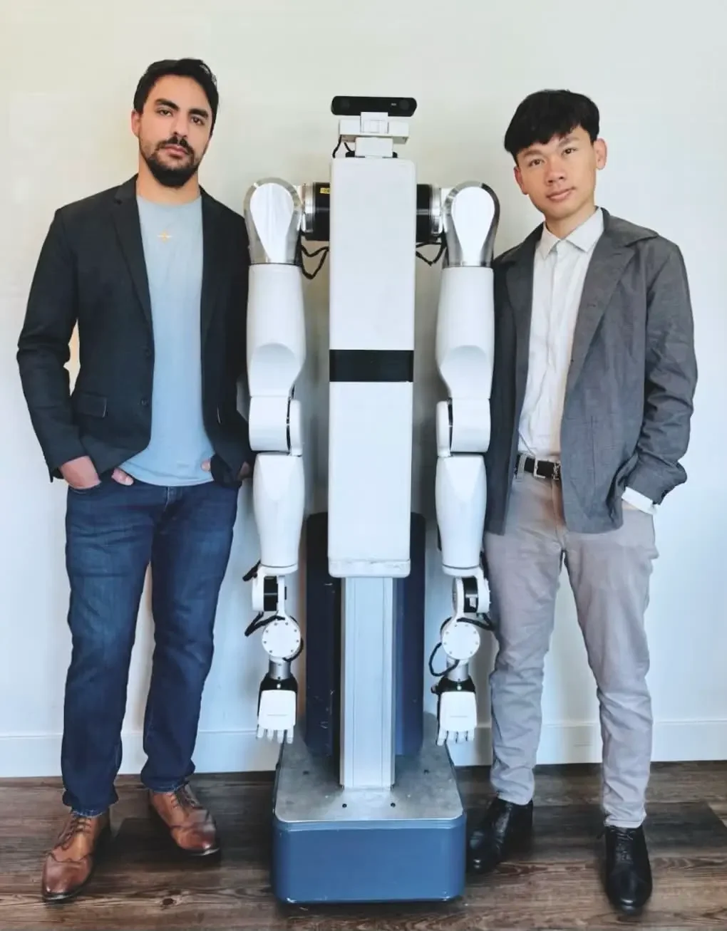 Two Feather team members standing on either side of the wheeled, dual-arm robot.