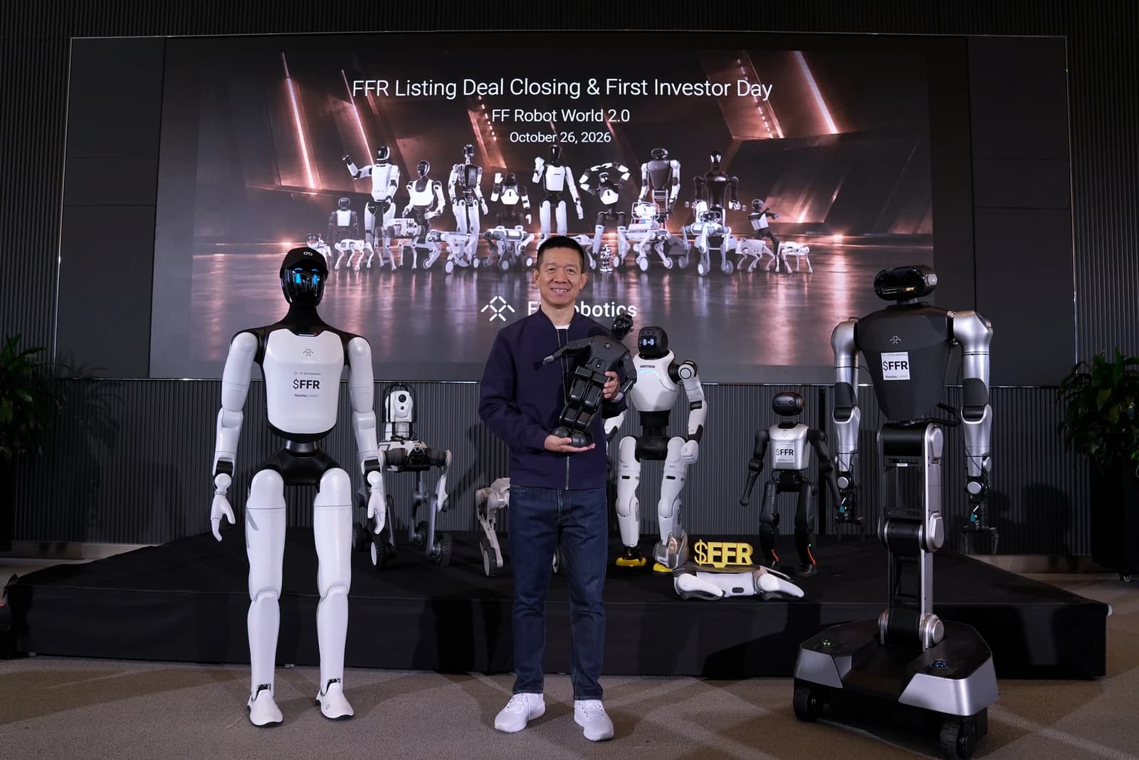 A presenter holds a small robot among humanoid, wheeled and quadruped robots at the FFR deal closing and Investor Day event.