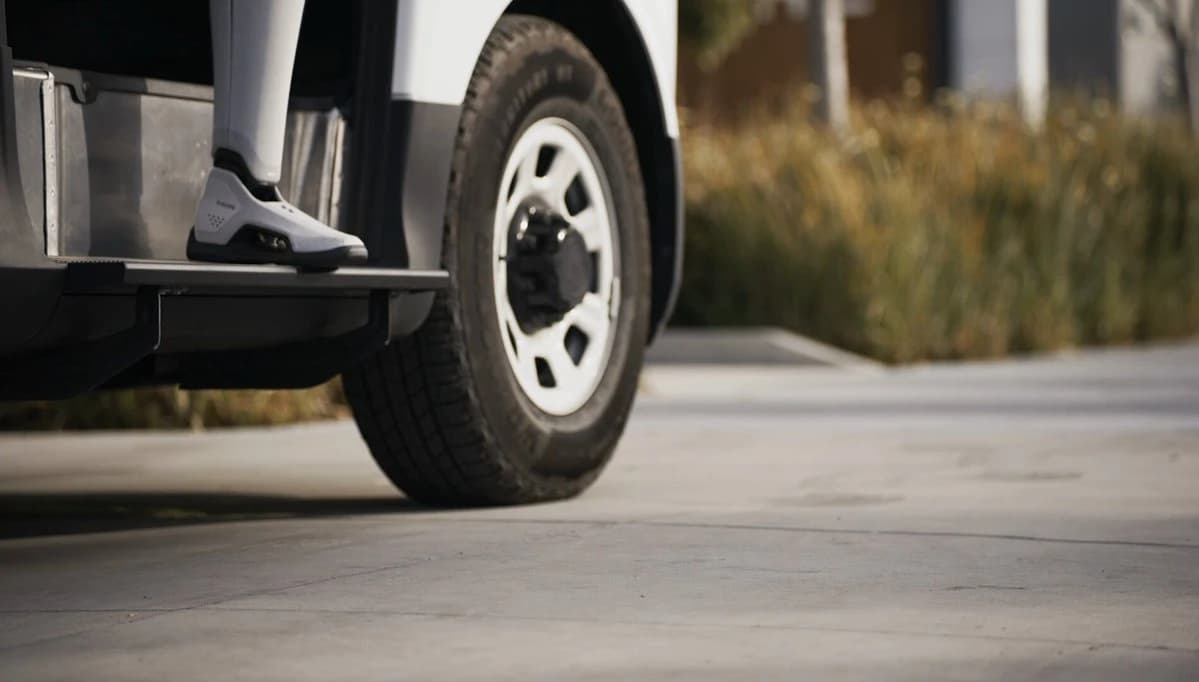 A Figure robot's lower leg and foot on the step of an open vehicle doorway.