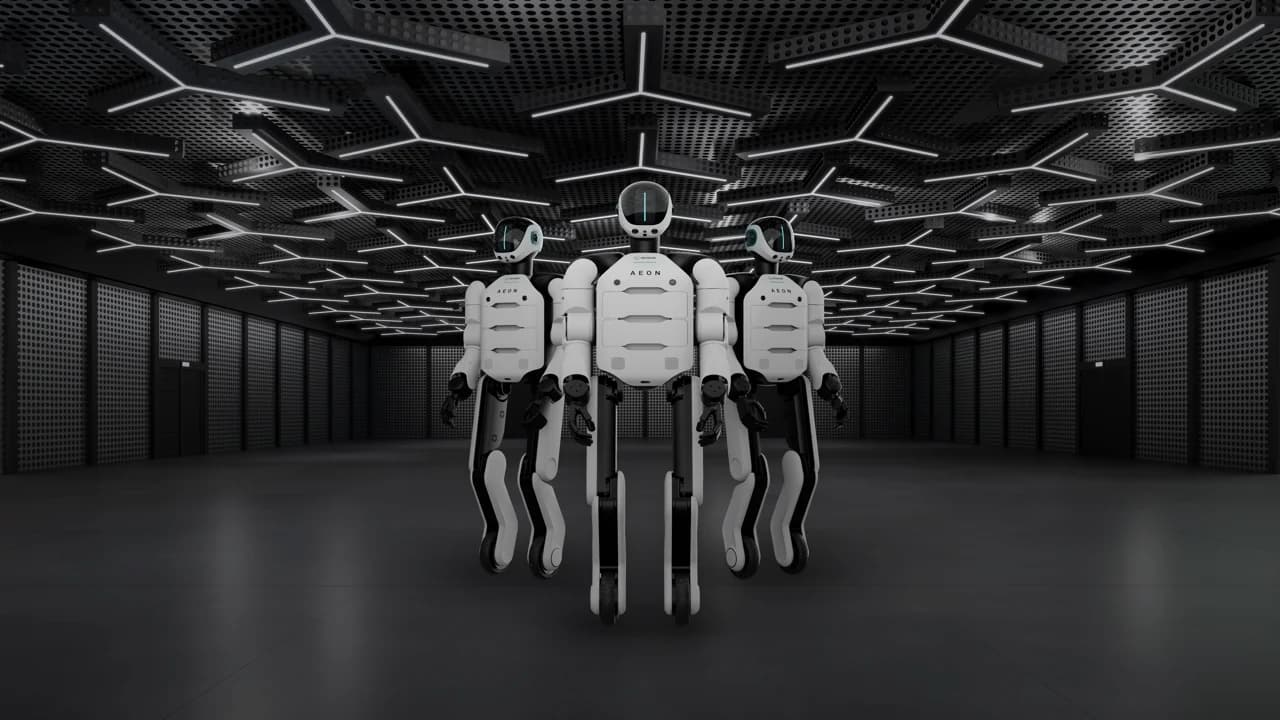 Three Hexagon AEON humanoids standing together in a dark hall beneath a ceiling of illuminated hexagonal light bars, their white and black panelled bodies carrying the AEON wordmark on the chest, visored heads lit by a thin green line, and articulated legs ending in wheels rather than feet.