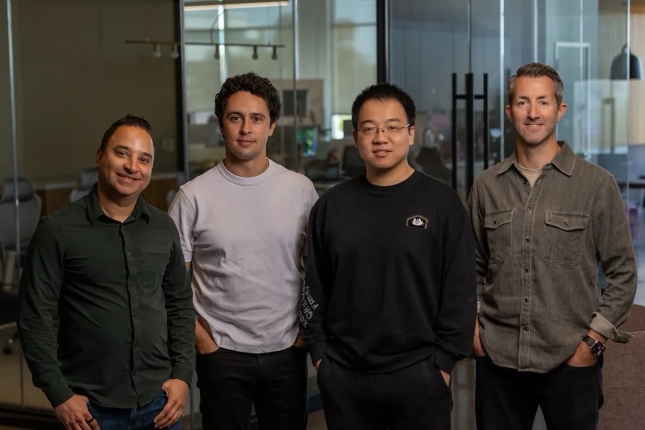 Four men standing side-by-side in a modern, glass-walled office setting. From left to right: Pally Kumar, Theophile Gervet, Zhou Xian, and Damien Kieran.