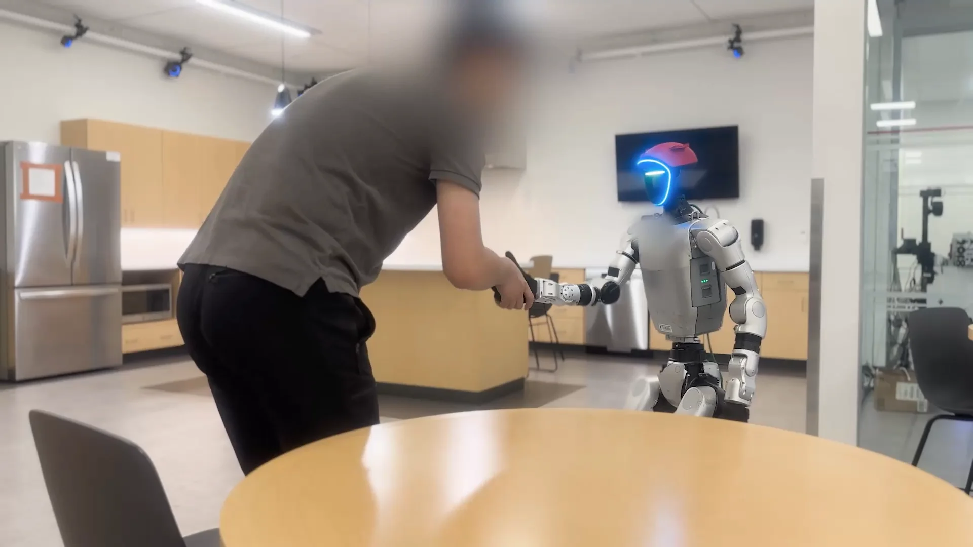 A person and a Unitree G1 humanoid robot are engaged in a handshake, illustrating a safe and compliant physical interaction between a human and the machine.