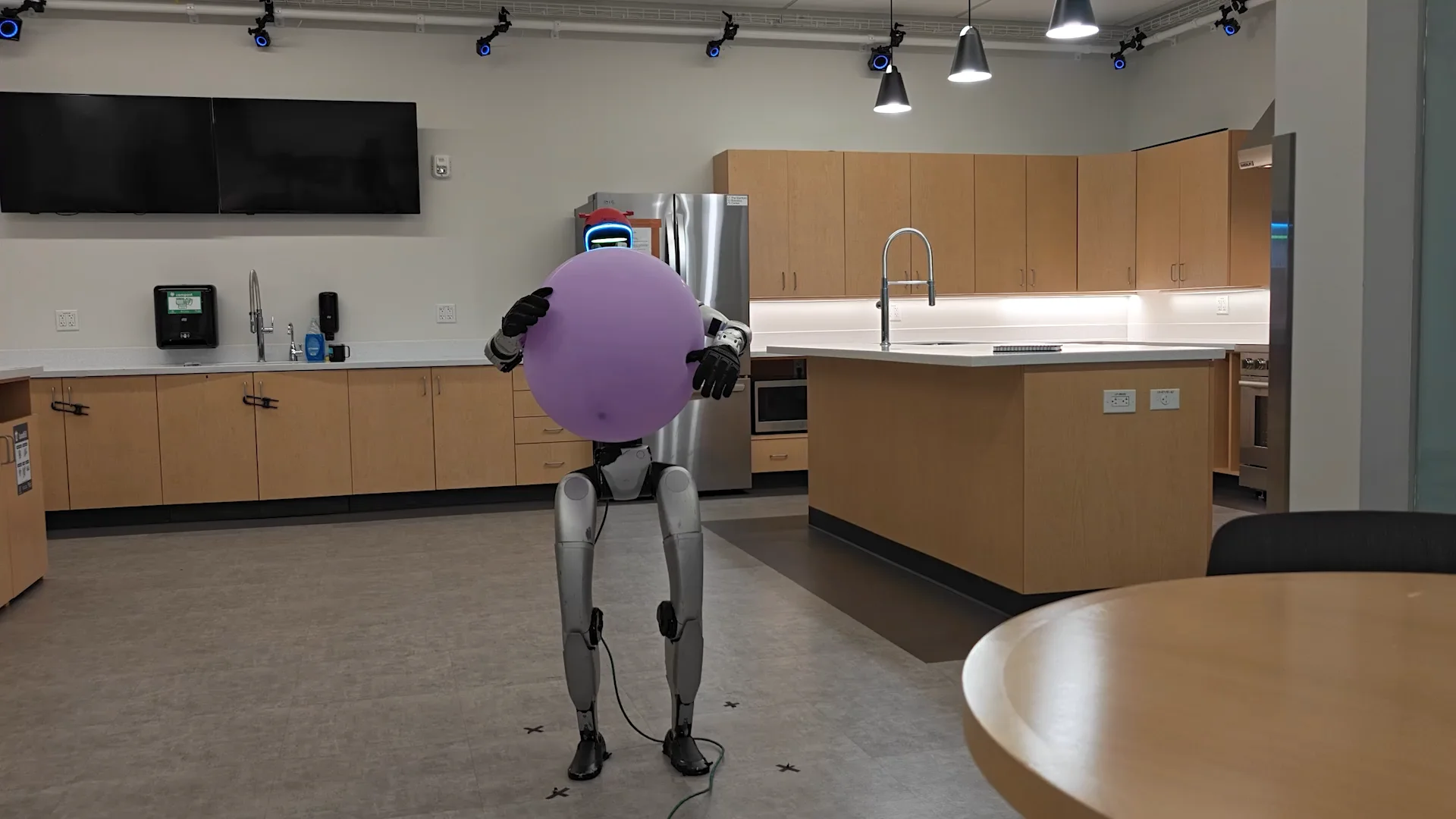A Unitree G1 humanoid robot holds a large, fragile balloon between its two hands, demonstrating its ability to apply gentle, controlled force to a delicate object