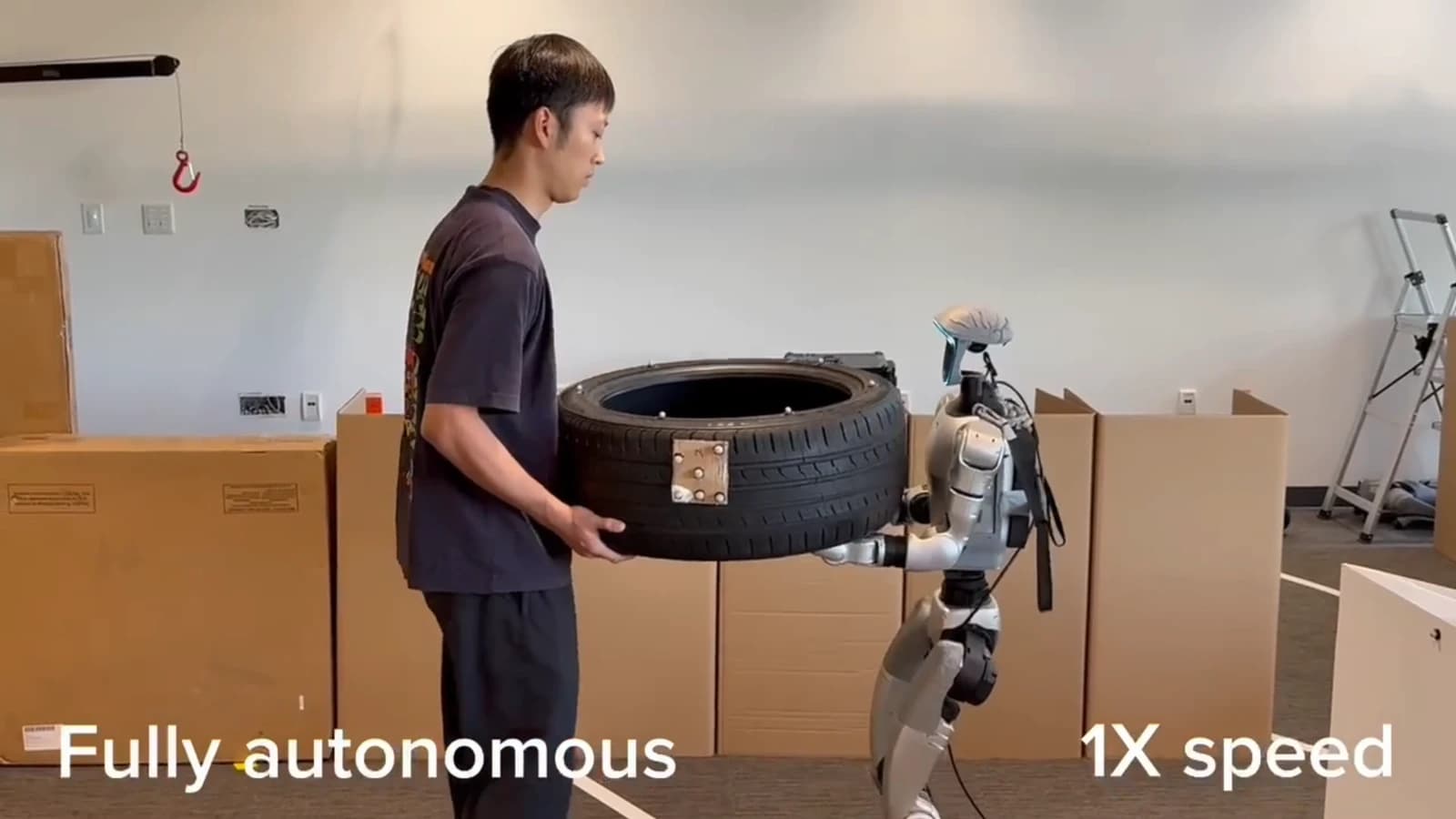 A person and a Unitree G1 humanoid jointly carrying a tire through a laboratory obstacle course.