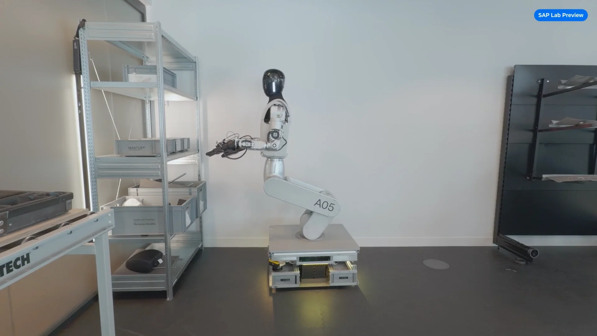 The Humanoid HMND-01 robot, a wheeled humanoid platform, uses its grippers to perform a picking task in an industrial setting, moving components from a bin to a container.