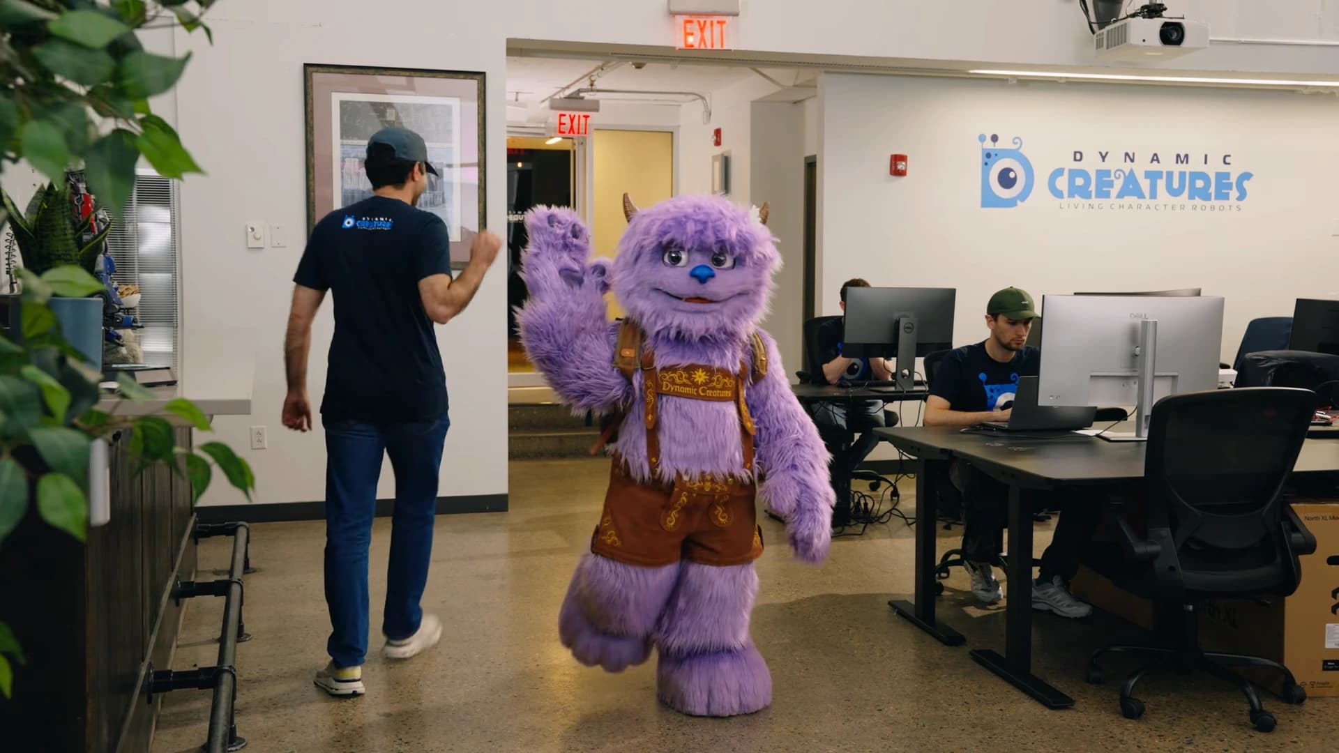 Hugo, a purple furry character robot, raises a hand in the Dynamic Creatures office.