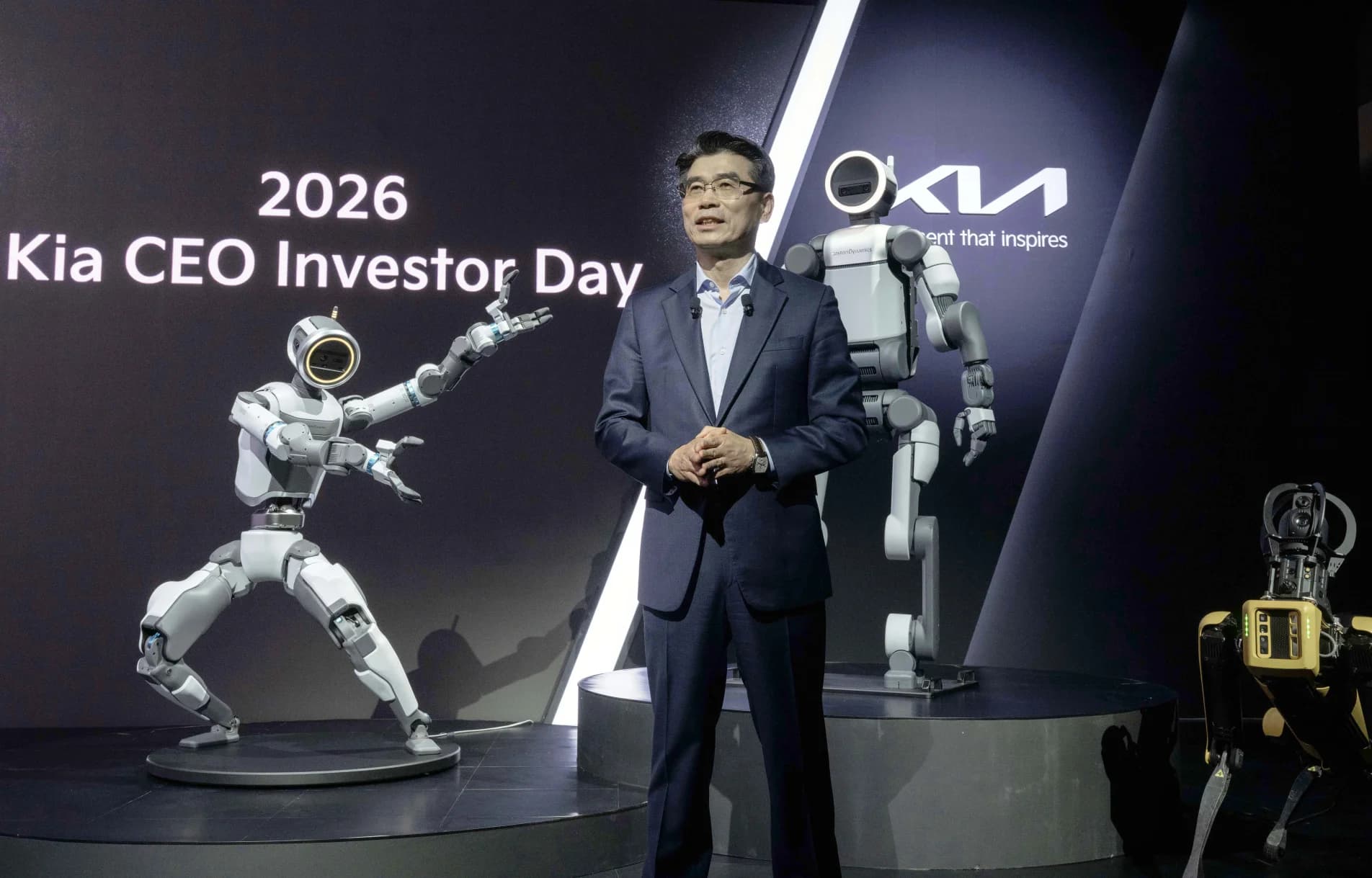 Kia President and CEO Ho Sung Song standing center stage with two Atlas humanoid robots and a Spot quadruped robot during the 2026 Kia CEO Investor Day.